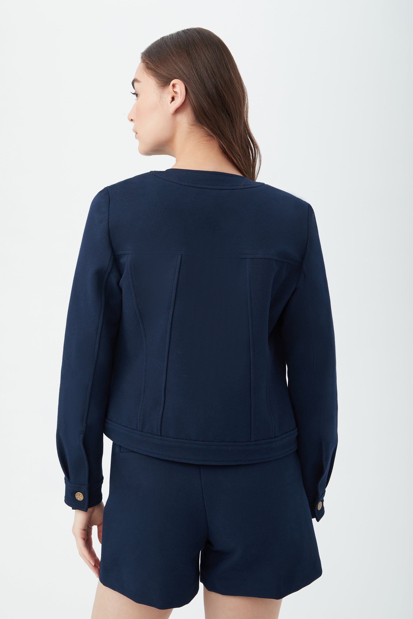 A woman with long brown hair is seen from the back wearing the Gail Jacket in navy blue and matching shorts, standing against a plain white background.