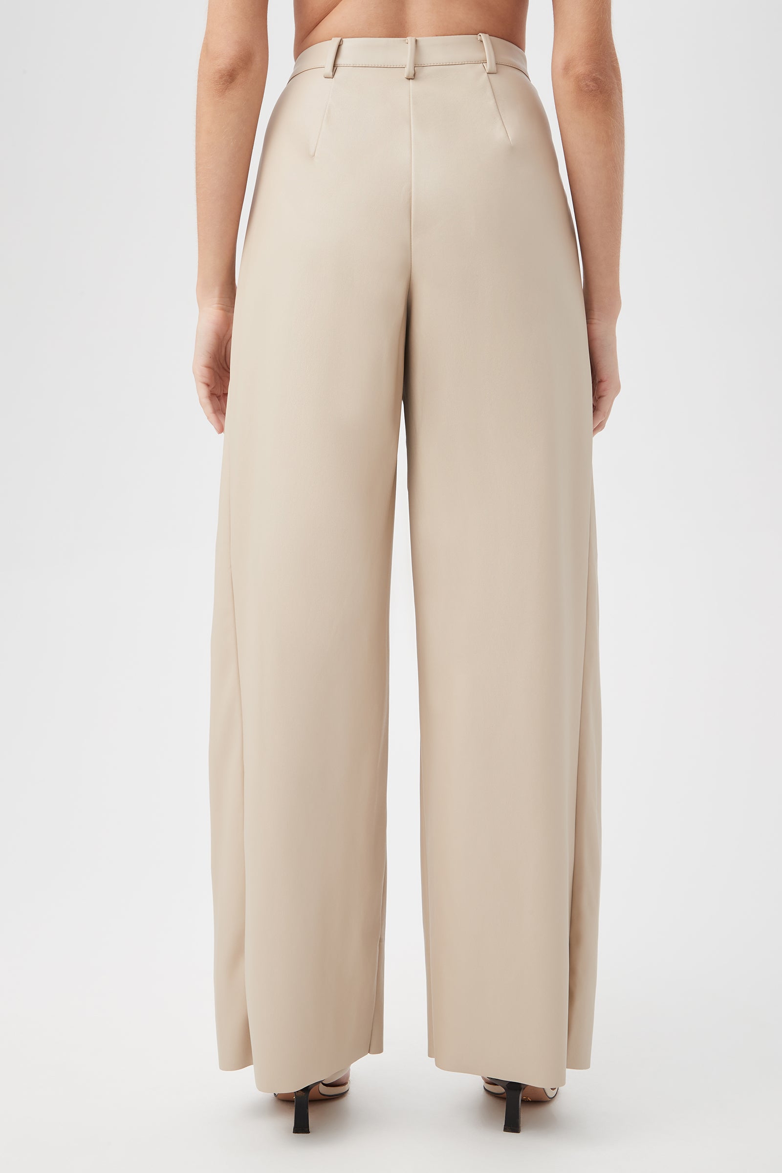 A person wearing the Bexley Pant, high-waisted wide-leg beige trousers, is photographed from the back (mid-back down), with black heeled sandals visible.