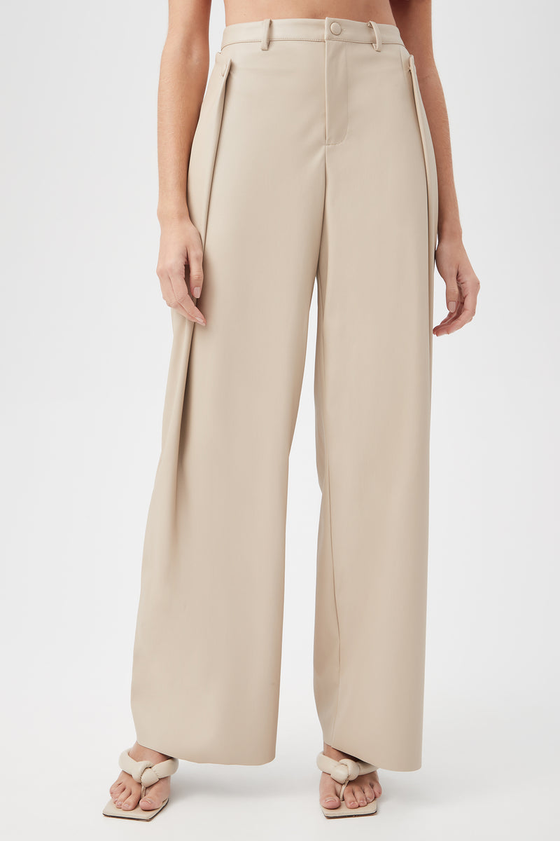 A person models the Bexley Pant in Chai—high-waisted, wide-leg trousers—paired with light sandals, standing against a plain white background. Only their lower torso and legs are visible.