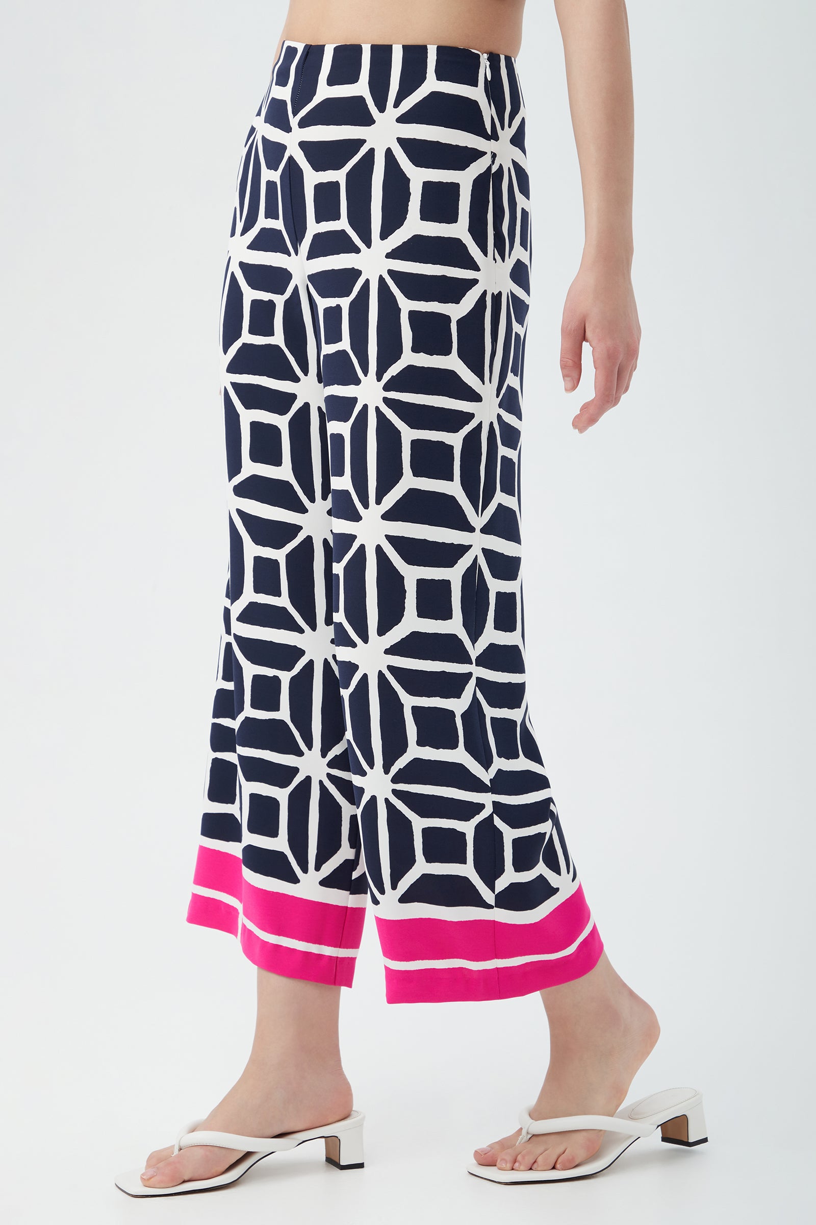 A person wears the Orlett Wide-Leg Crop Pant - Durell Georgette, featuring a navy blue and white geometric pattern with a bright pink and red hem, paired with white heeled sandals.