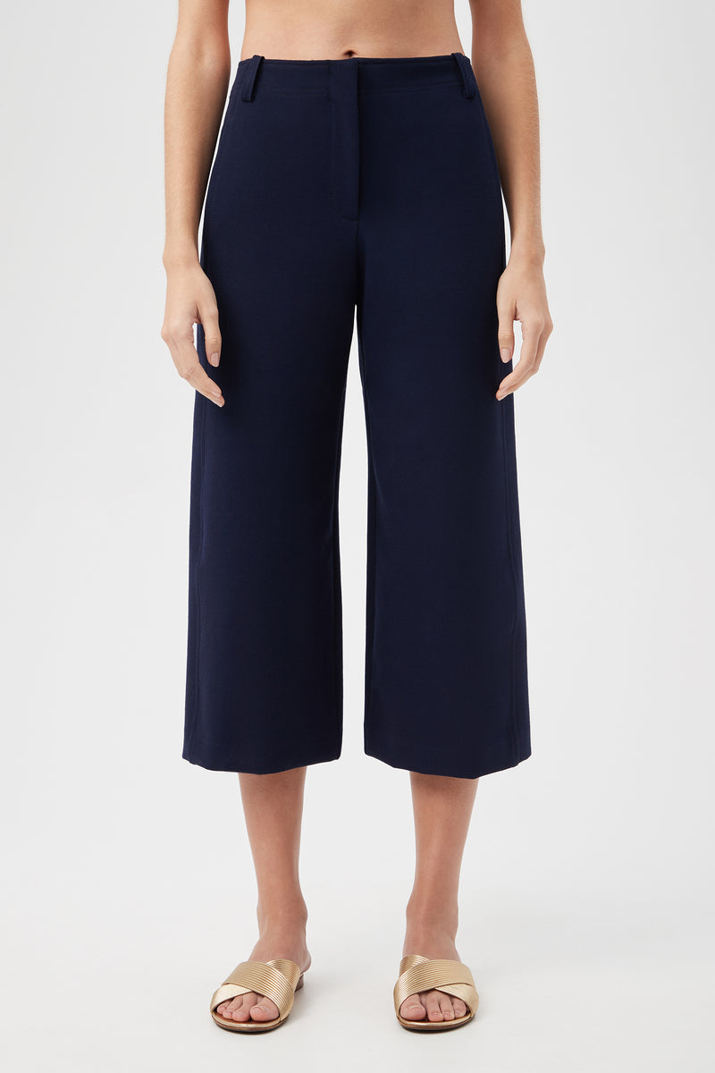 Model wears the Patyn Pant in indigo with light sandals, standing against a white background. The image is cropped at the chest and feet.
