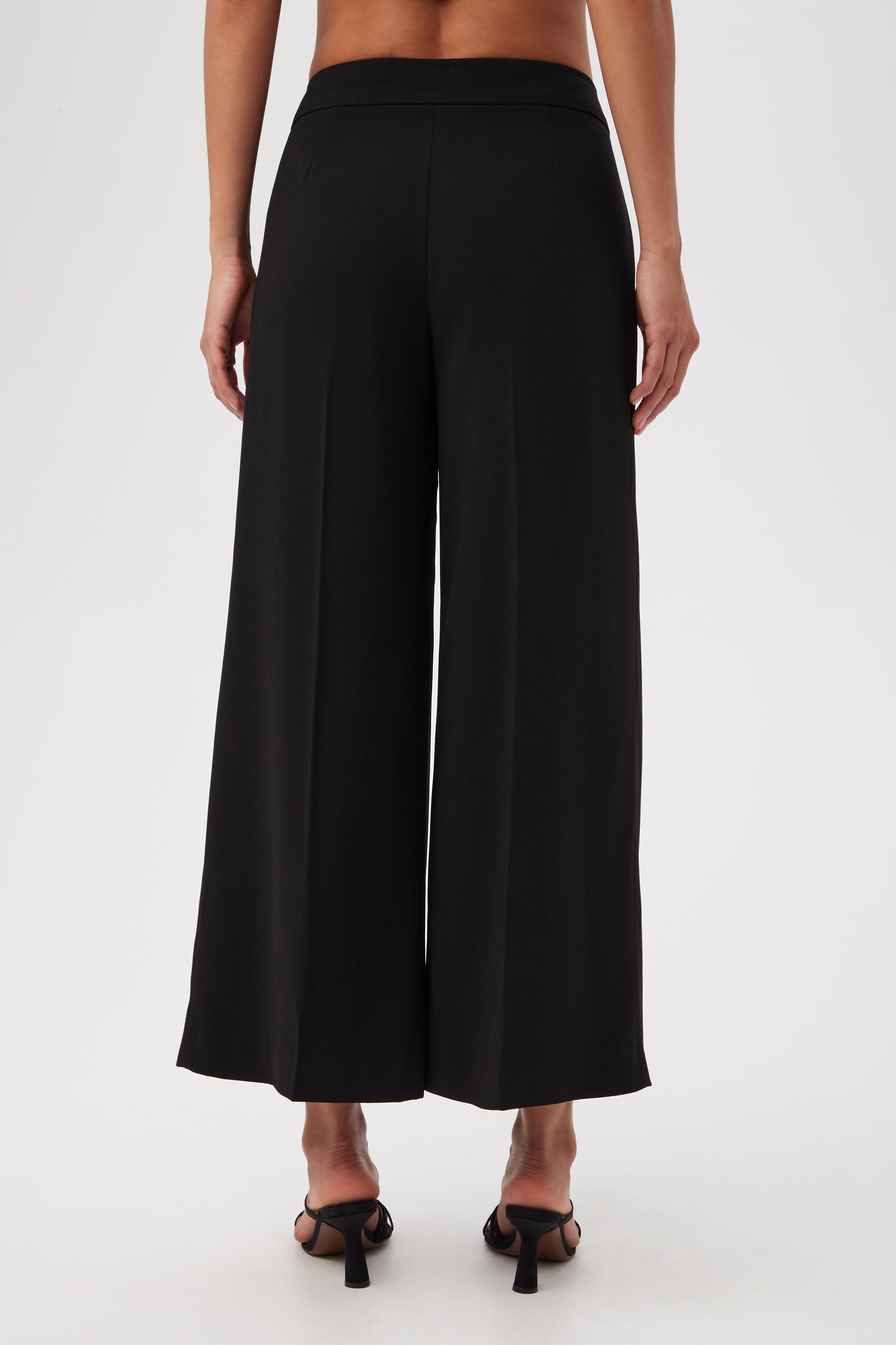 A person is shown from the back wearing Davon Cropped Wide-Leg Pants With Front Slits and black heeled sandals, set against a plain white background.