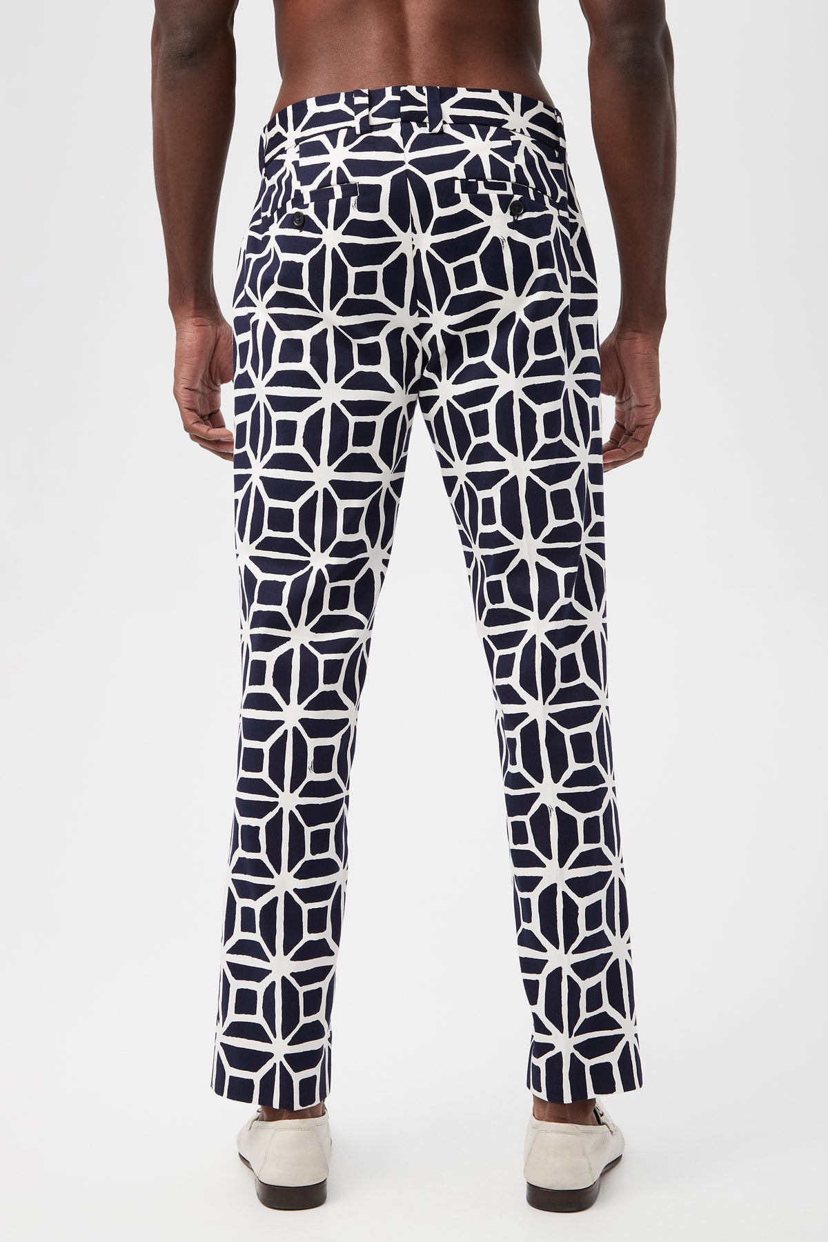 A man faces away, wearing the Clyde Slim Trouser in Durell Herringbone with a navy and white geometric pattern and light shoes, set against a plain white background.