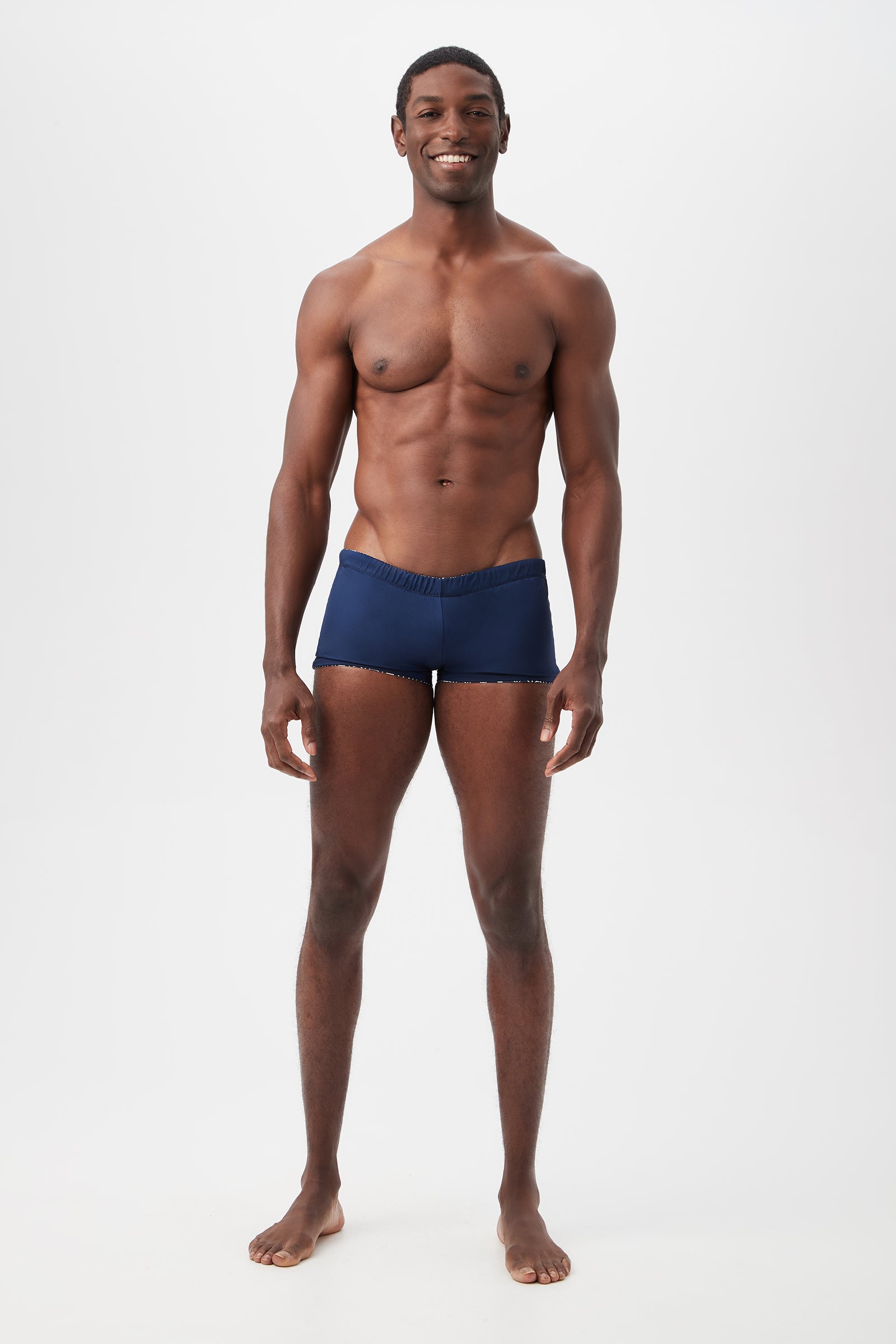 A smiling man stands against a plain white background, wearing the Seaside Reversible Swim Trunk in Durell Print.