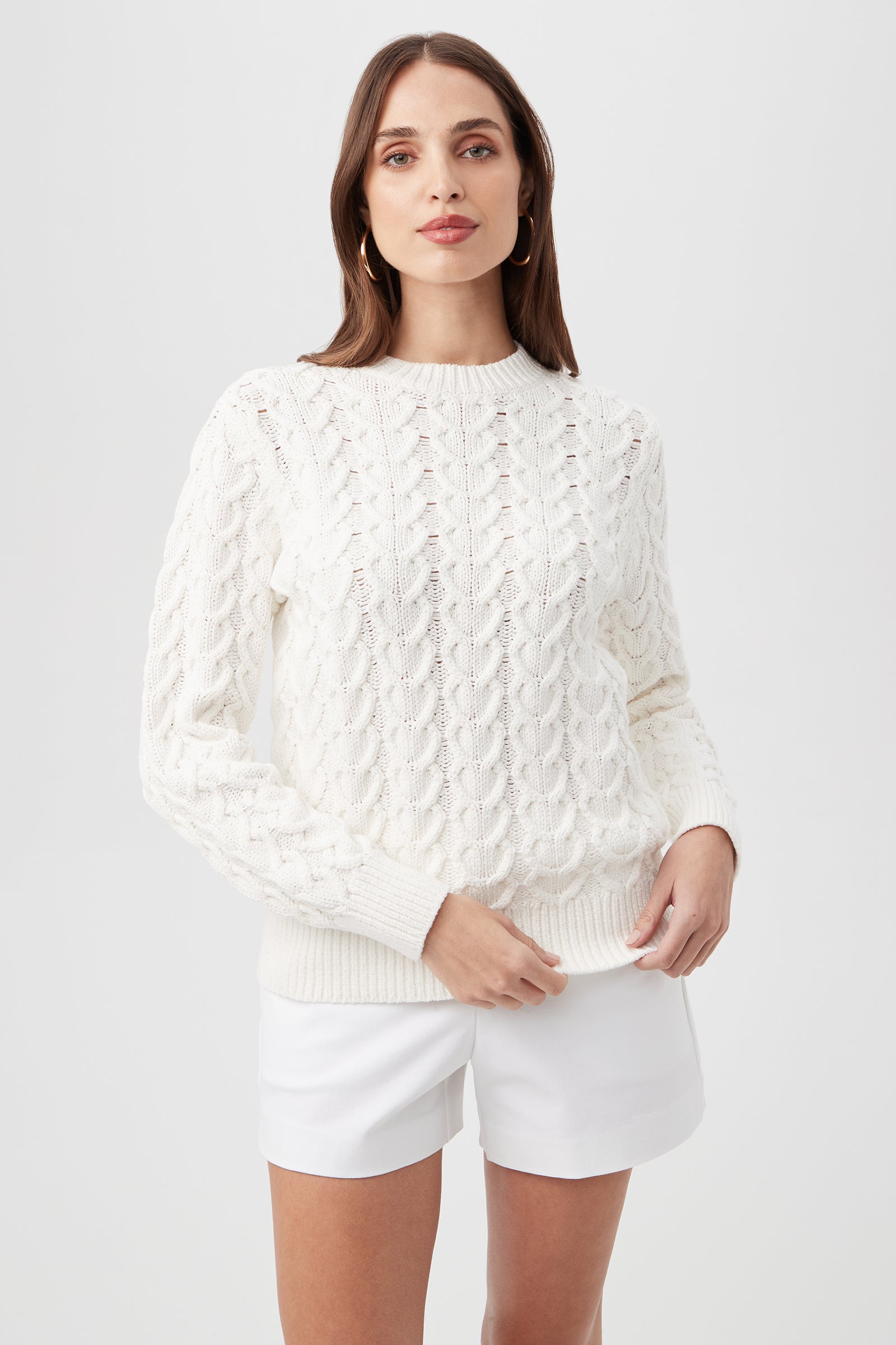Model wears the Corazon Heart Knit Crewneck Sweater in Whitewash with white shorts, standing against a light background and looking forward with a neutral expression.