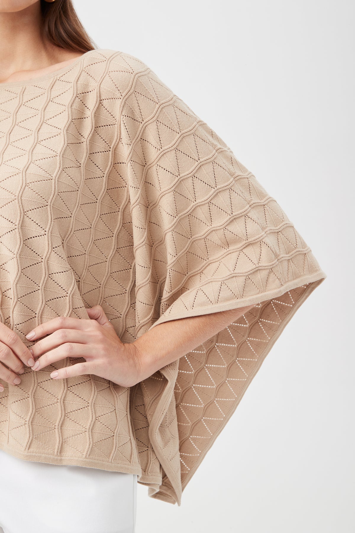 A person wears the Chic Wrap 2 Sweater—a beige, textured, geometric-patterned poncho with wide sleeves. Only their upper body and part of the arm are visible against a plain light background.