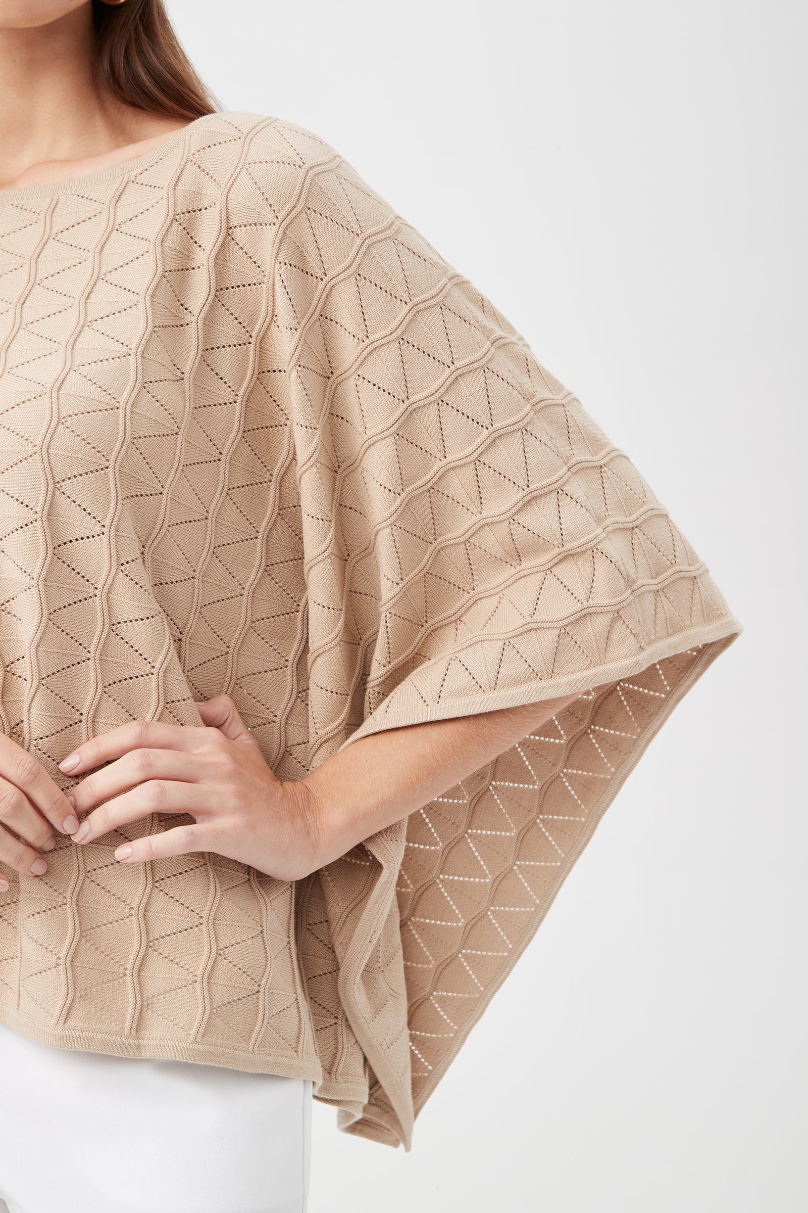 A person wears the Chic Wrap 2 Sweater—a beige, textured, geometric-patterned poncho with wide sleeves. Only their upper body and part of the arm are visible against a plain light background.