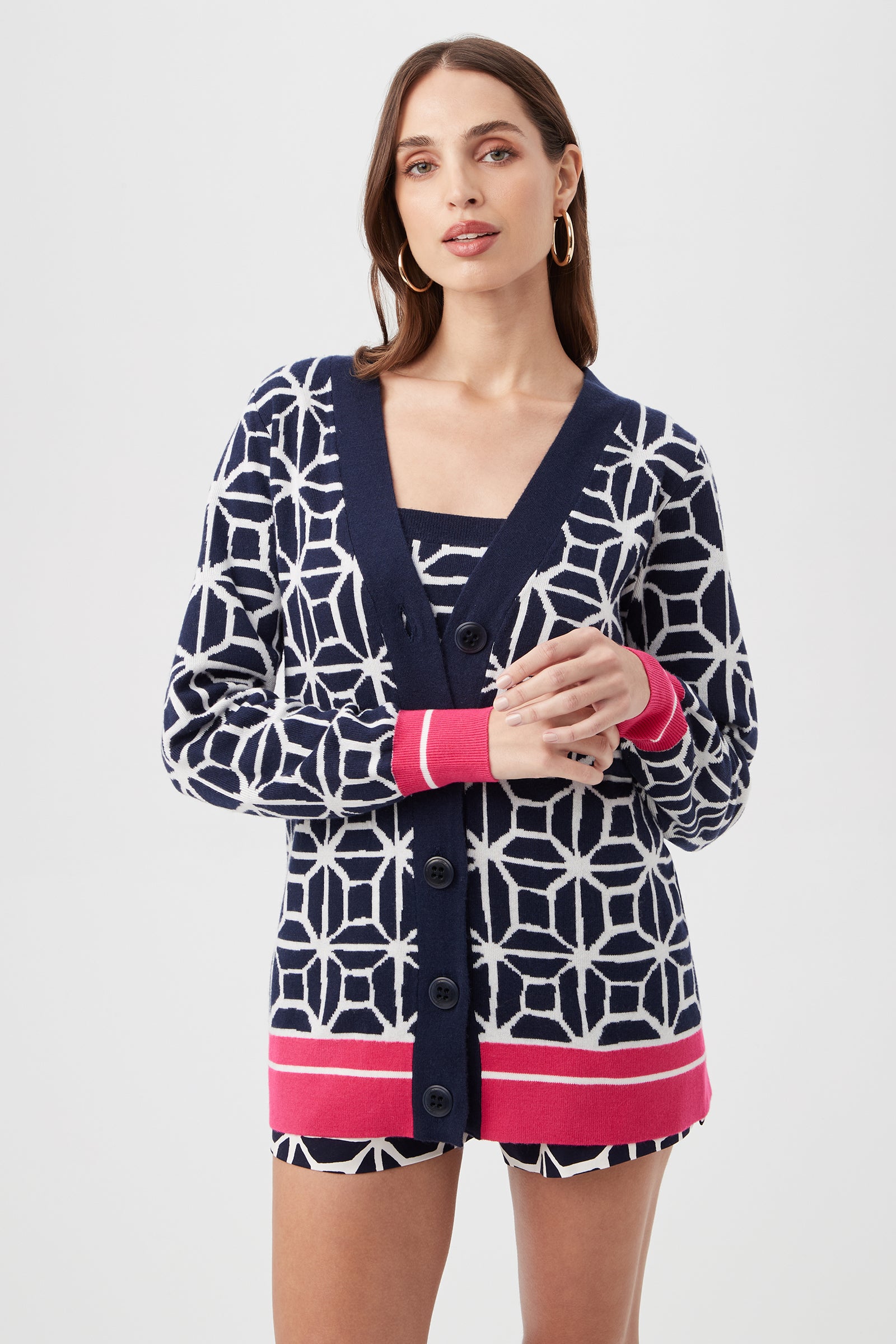 A woman with long brown hair and hoop earrings wears the South Bay V-Neck Cardigan - Durell Knit in Multi over a matching top, standing against a plain light background.