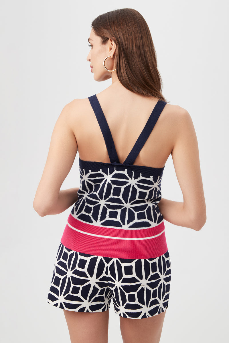 A woman with long brown hair, shown from the back against a plain light background, wears the Casady Sleeveless Cami Top - Durell Knit paired with matching geometric navy and white shorts featuring a wide pink waistband.