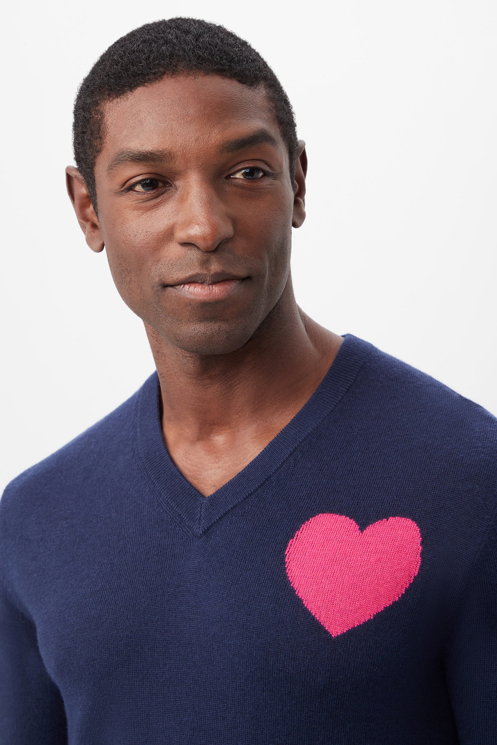 A man models the Lover Heart V-Neck Sweater, featuring a large pink heart on the left chest, against a white background.