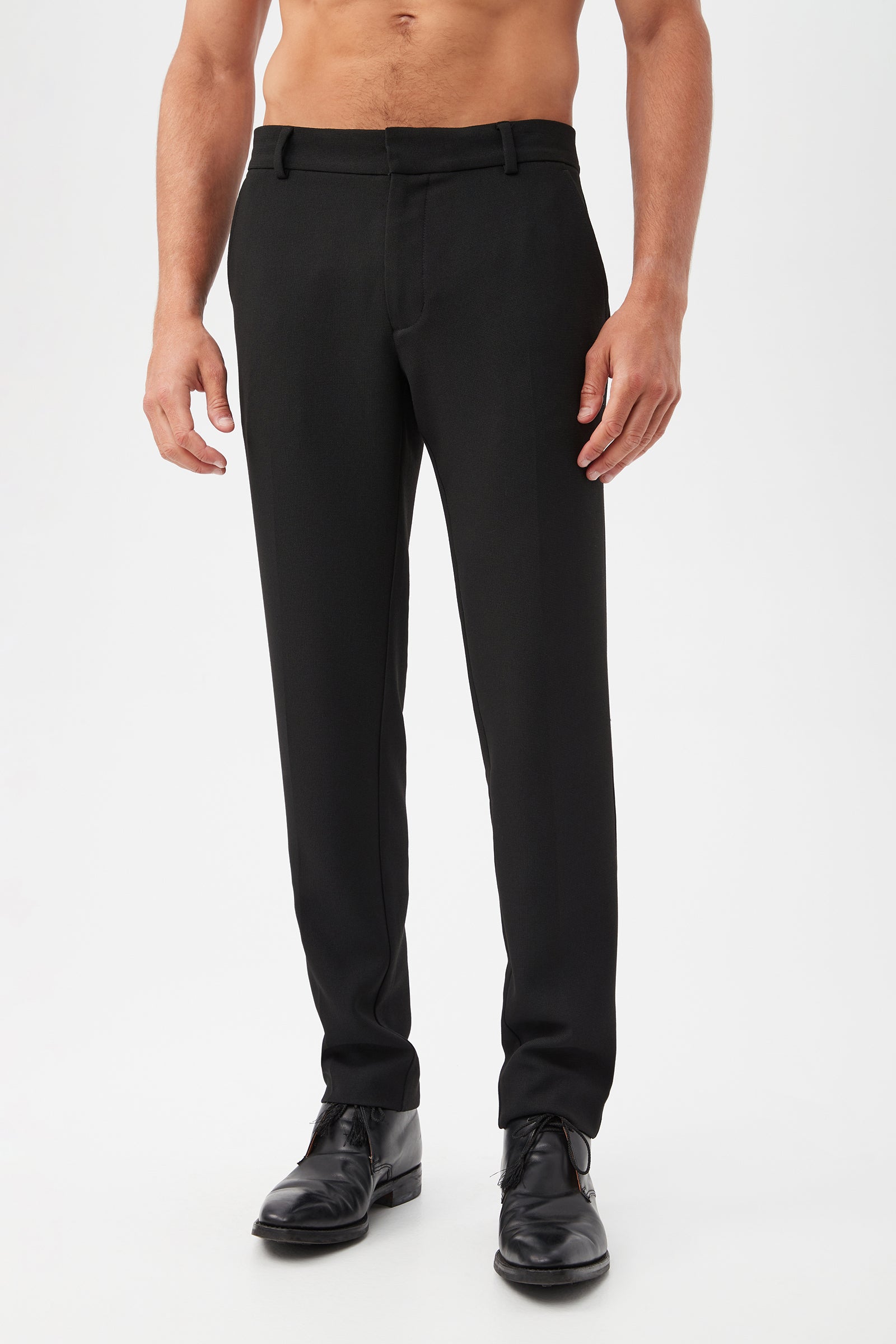 A shirtless man stands against a plain white background, hands relaxed at his sides, wearing the Clyde Slim Trouser - Hi-Line Suiting in black and black dress shoes.