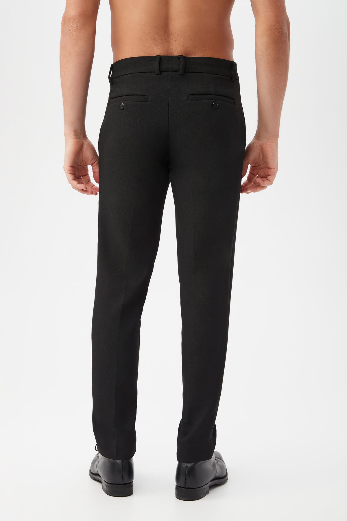 A shirtless man, seen from behind, models the Clyde Slim Trouser - Hi-Line Suiting with dress shoes against a plain white background.
