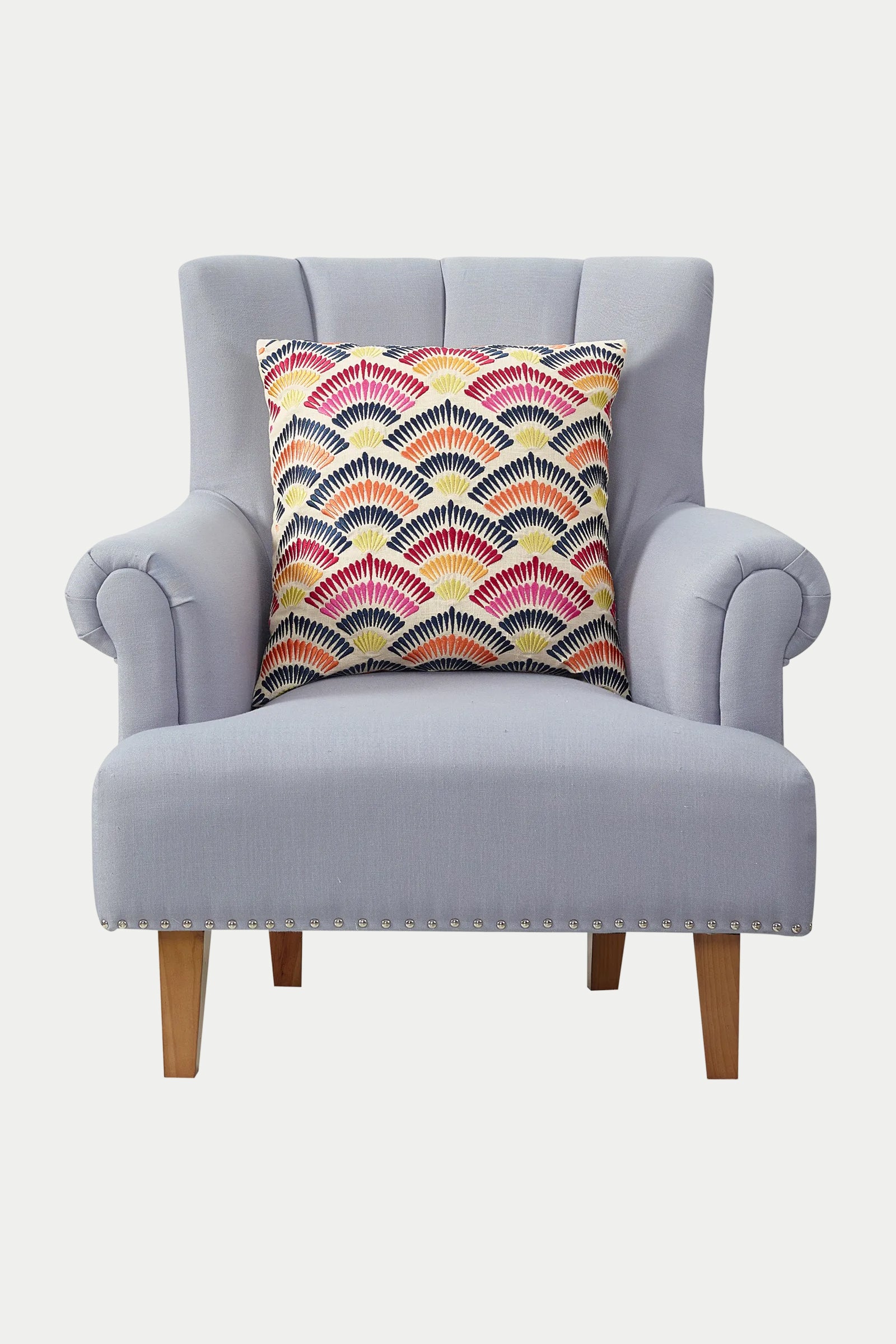 A light gray upholstered armchair with wooden legs features the Pasadena Embroidered Euro Throw Pillow in multi, showcasing a vibrant fan-shaped pattern in red, yellow, pink, blue, and white.