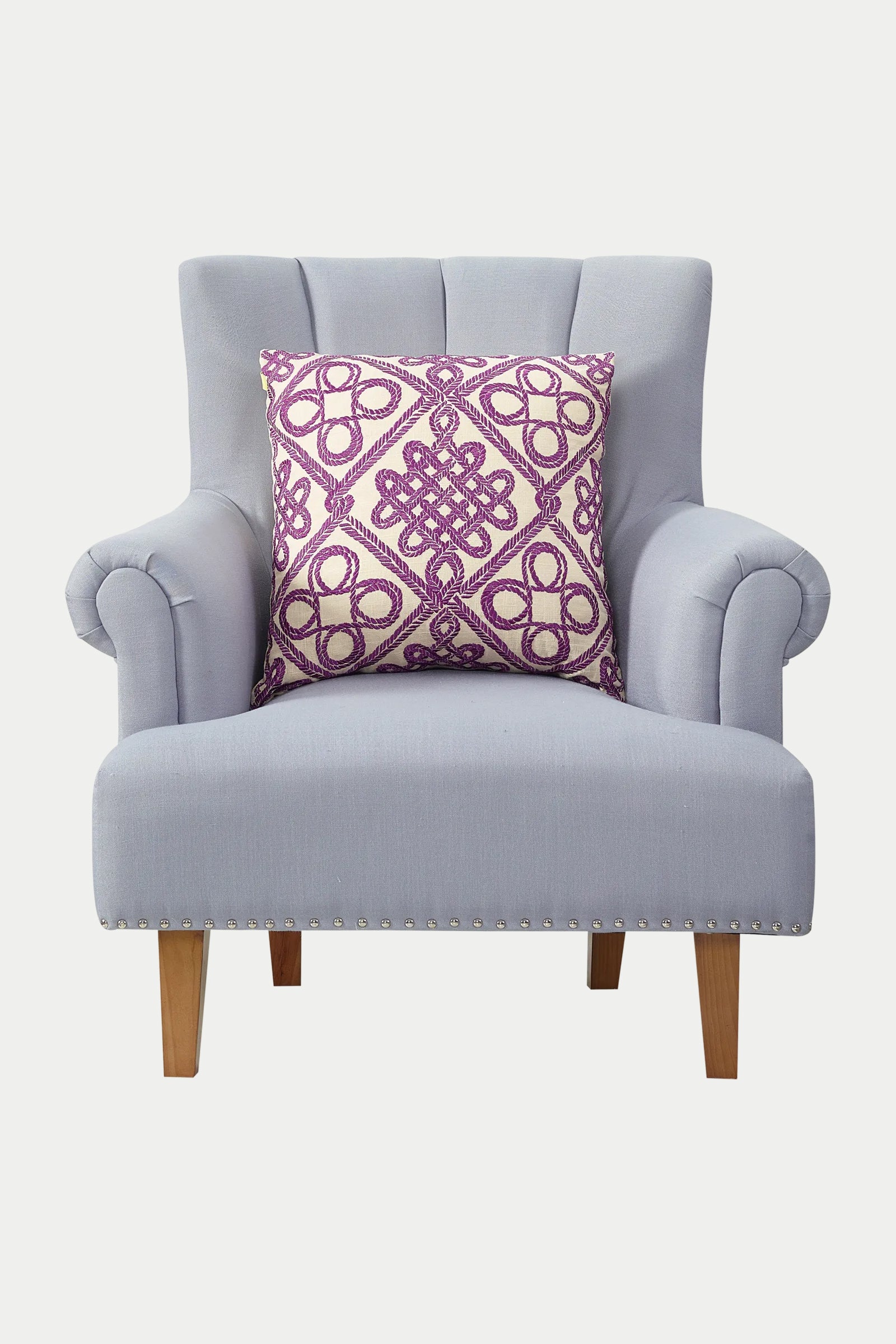 A light gray upholstered armchair with wooden legs, featuring the Costa Mesa Embroidered Euro Throw Pillow - Multi with a purple and white geometric pattern placed on the seat.