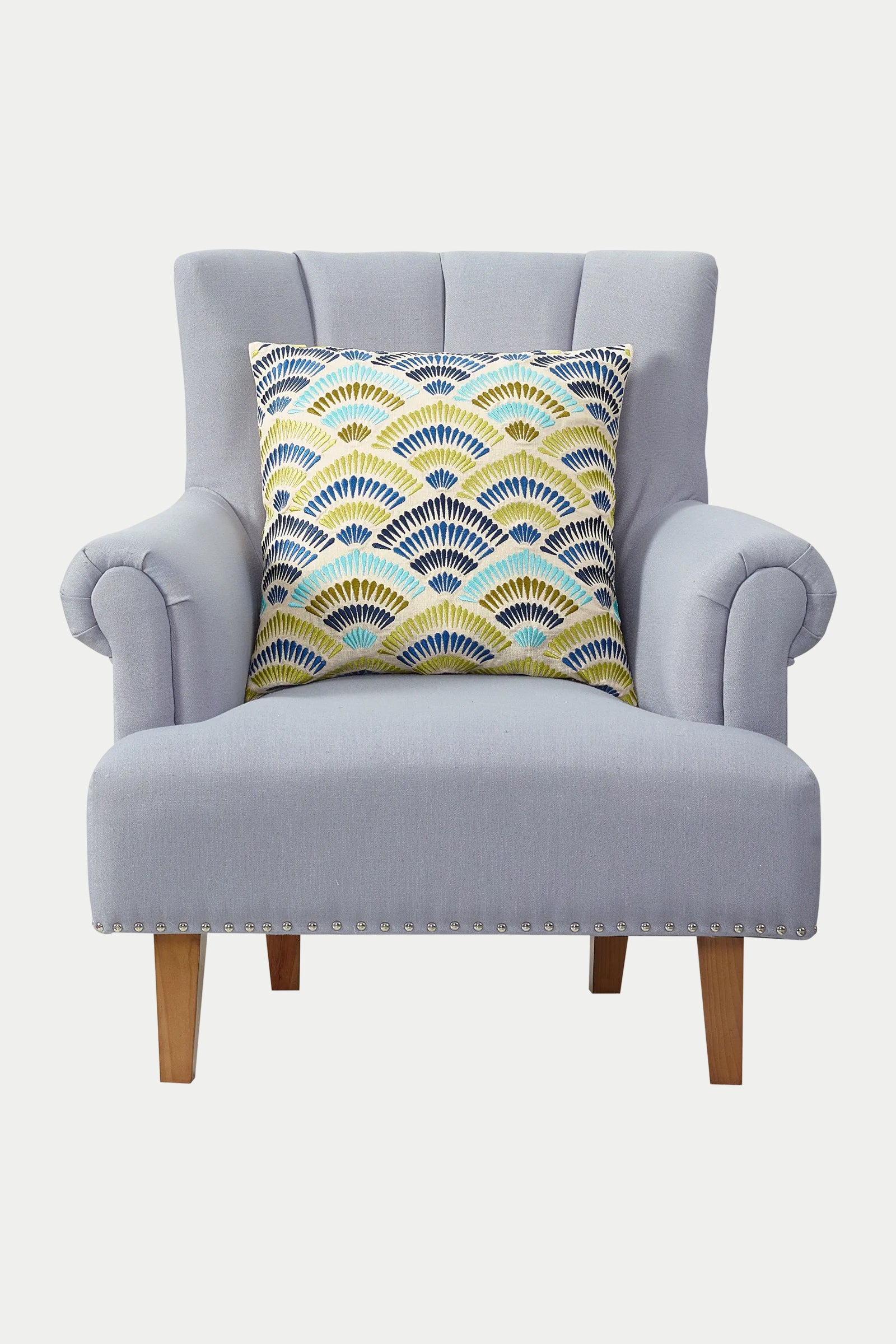 A light gray upholstered armchair with wooden legs, featuring the Pasadena Embroidered Euro Throw Pillow – Blue, placed at the center of the backrest.