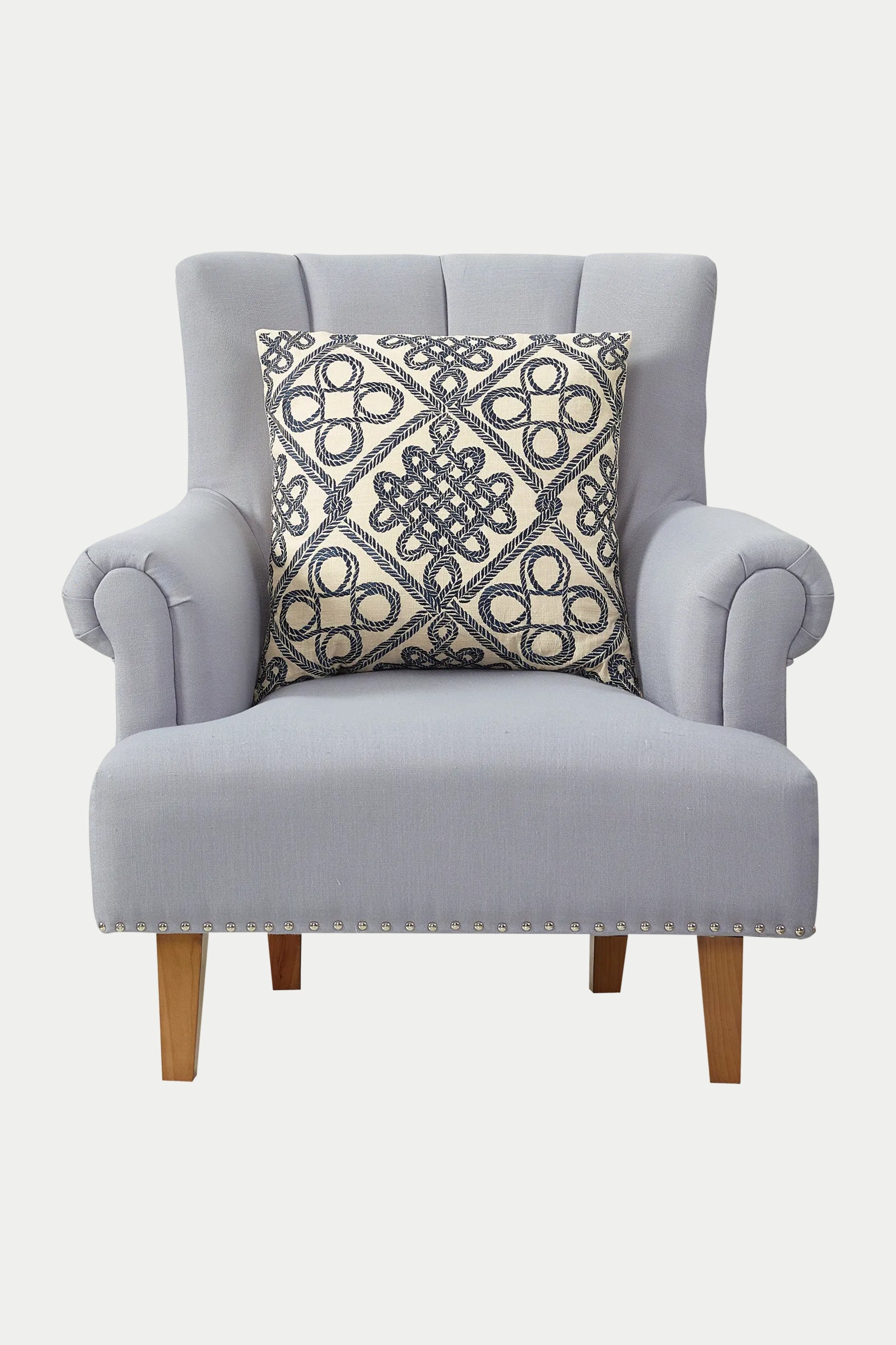 A light gray upholstered armchair with wooden legs features the Costa Mesa Embroidered Euro Throw Pillow in blue placed on the seat.