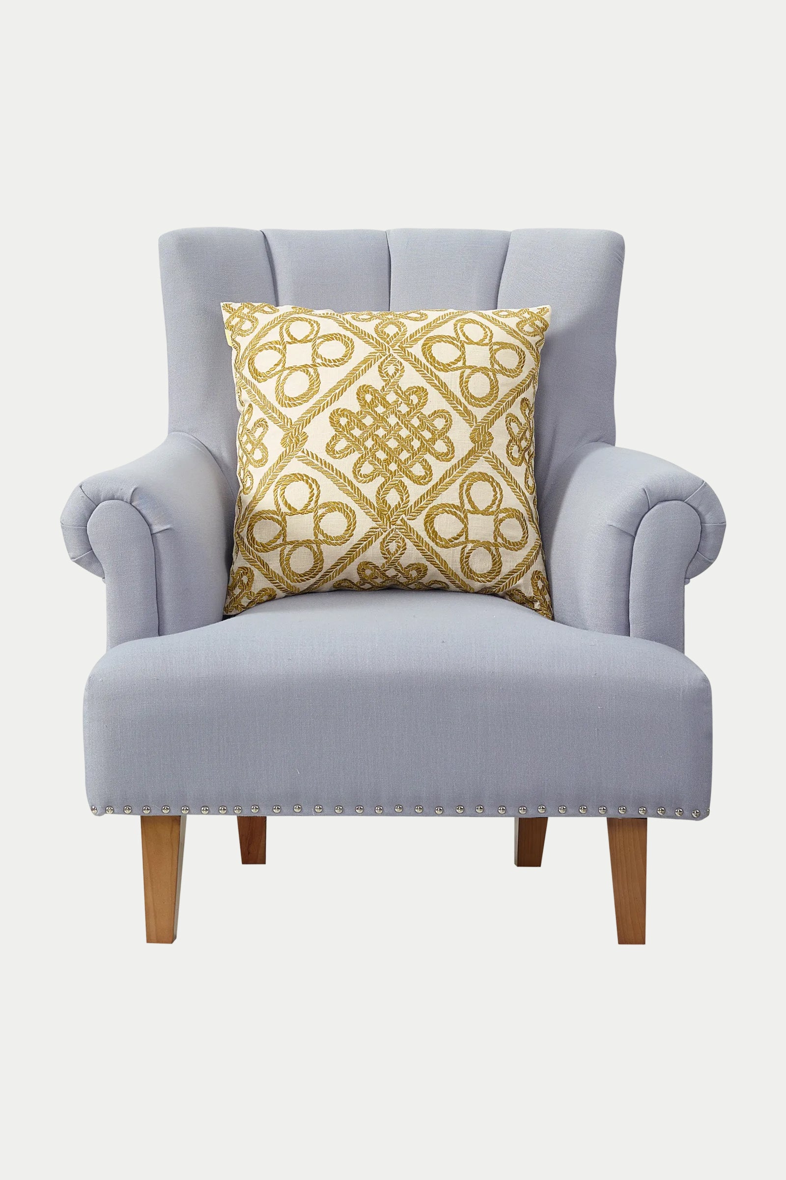 A light gray upholstered armchair with wooden legs and silver nailhead trim features the Costa Mesa Embroidered Euro Throw Pillow in gold placed on the seat.