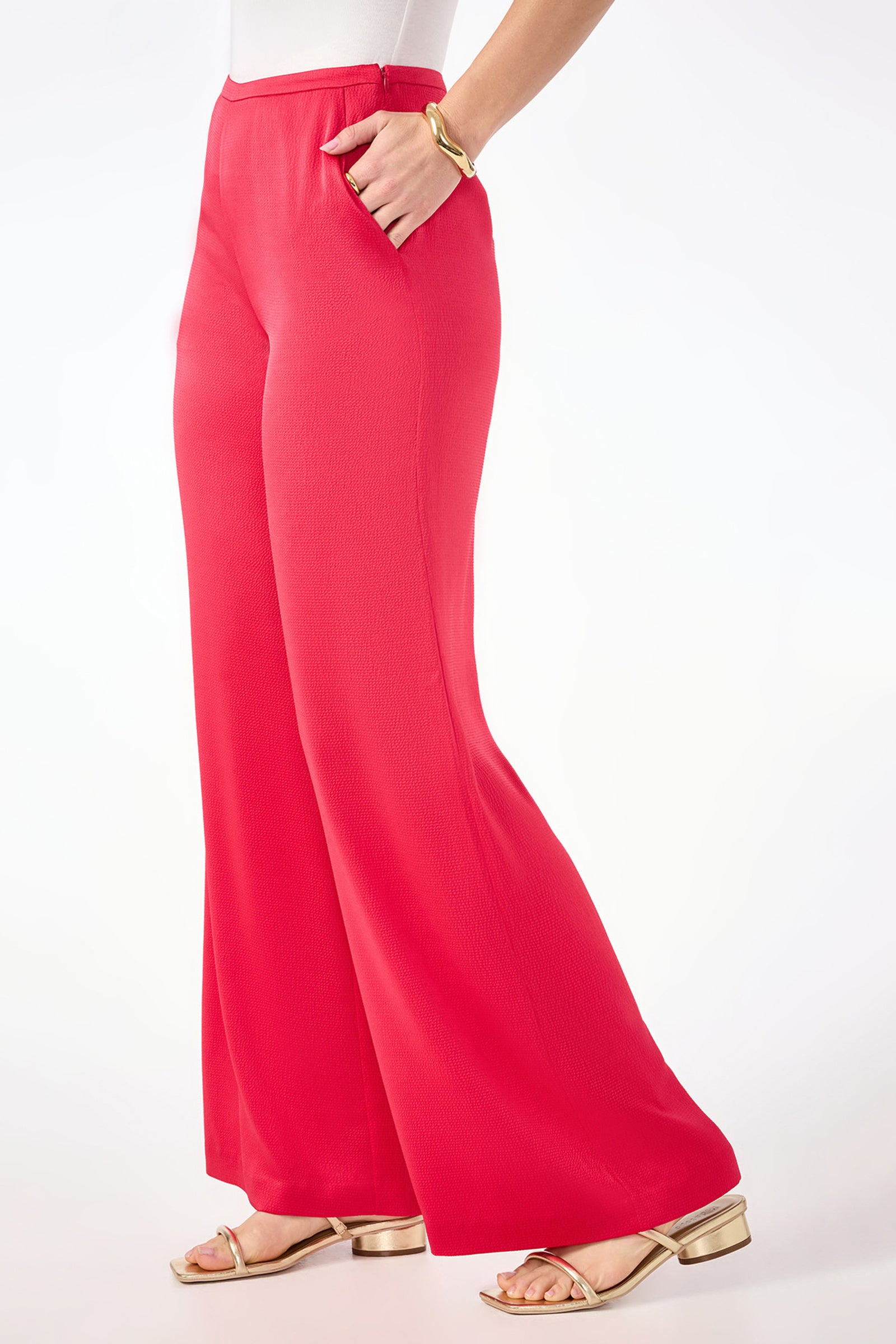 A person wears the Tavia Wide-Leg Pant in bright red hammered satin with a side zipper, styled high-waisted, paired with a white top, gold bracelet, and gold flat sandals against a plain white background.