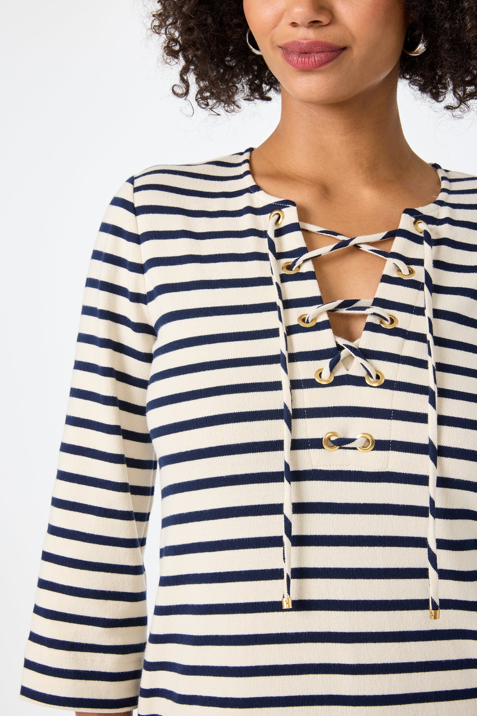 Woman wearing the Catamaran 3/4 Sleeve Maxi Dress in cream and navy blue stripes with a lace-up neckline and gold eyelets, shown from upper torso to mouth, smiling slightly.