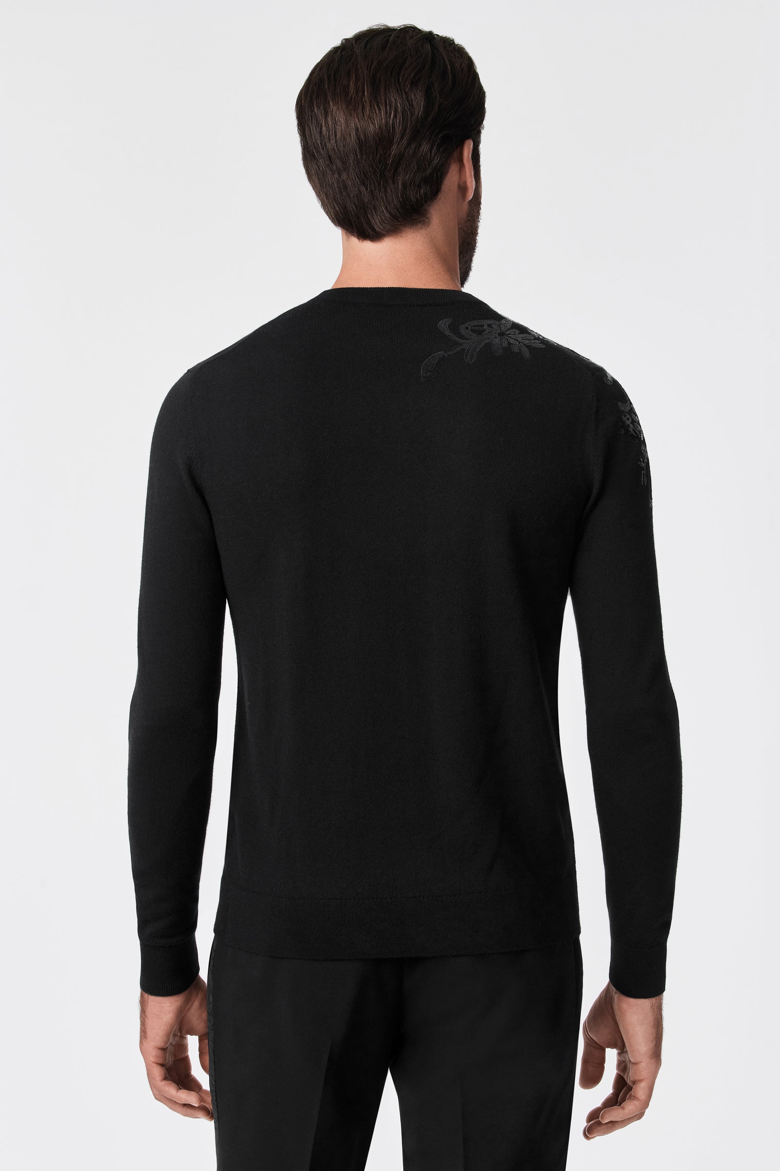 A man with short brown hair is seen from behind wearing the fitted, long-sleeve black Jaxon Sequin Crewneck Sweater and black pants against a plain white background.