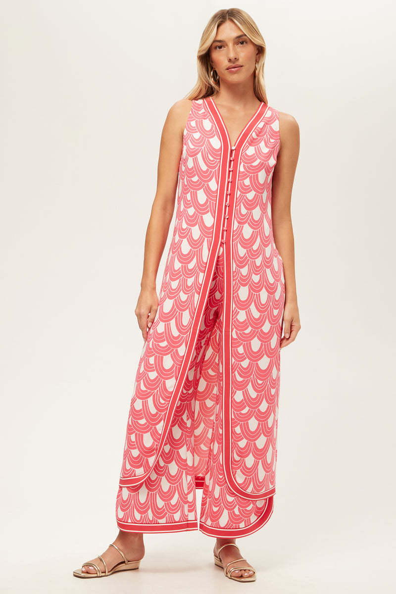 A woman in the Slice Sleeveless Maxi Top - Ace Arches in Coral Crush/Whitewash, featuring a V-neck, wide legs, and side slits, pairs it with flat sandals while standing against a plain light background.