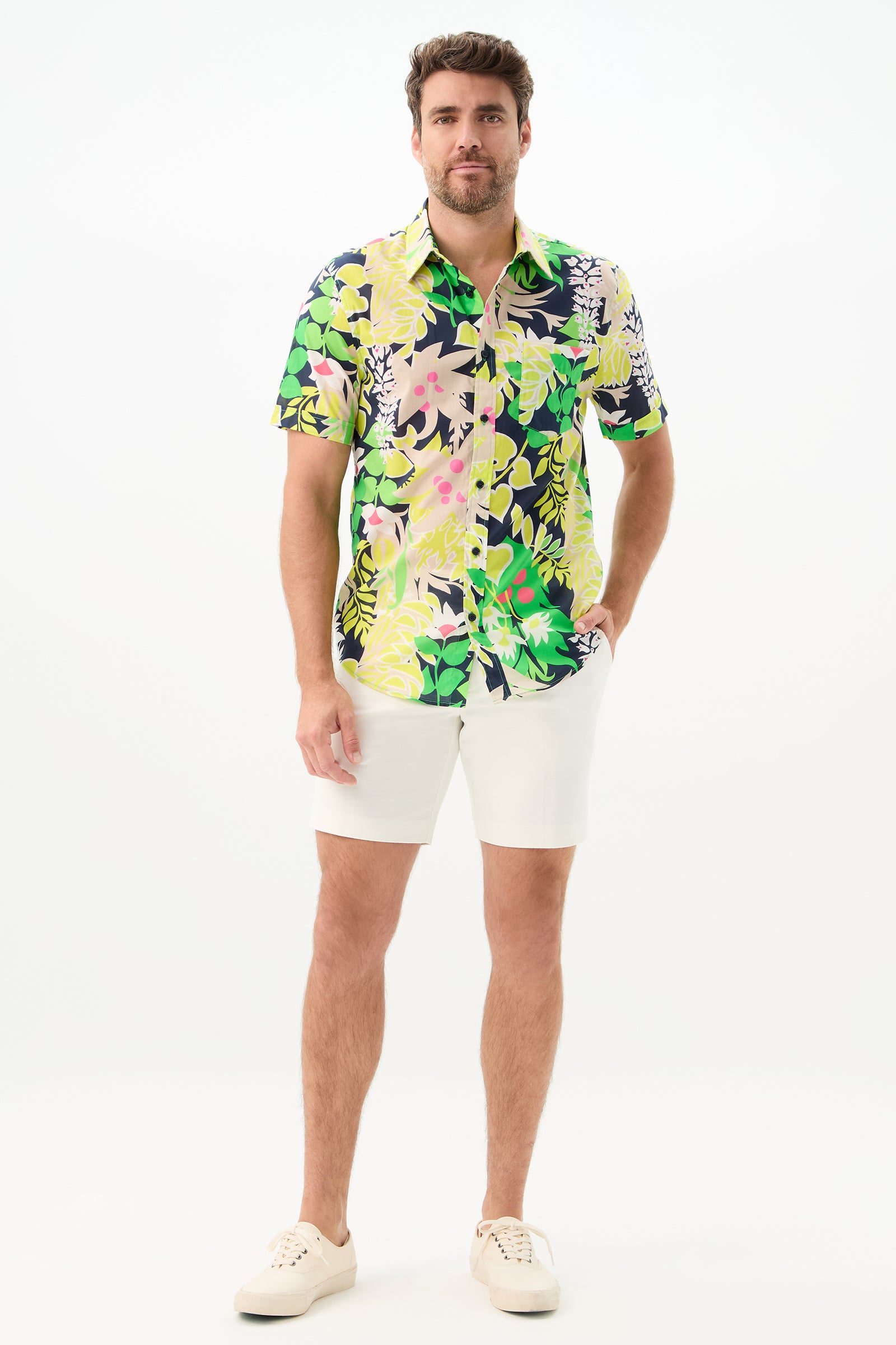 A man stands against a white background wearing the Slim Jim Short-Sleeve Shirt, paired with white shorts and sneakers, his left hand in his pocket and a relaxed expression.