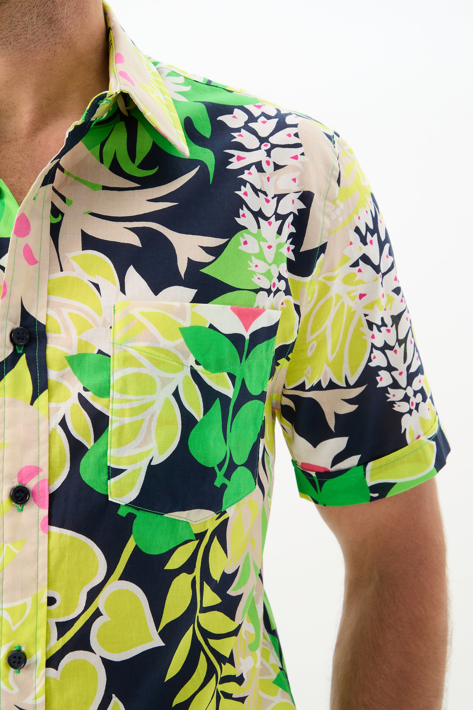 A close-up of a man wearing the Slim Jim Short-Sleeve Shirt, featuring a bold, colorful tropical leaf and floral pattern in green, yellow, navy blue, pink, and white. Only part of his face is visible.
