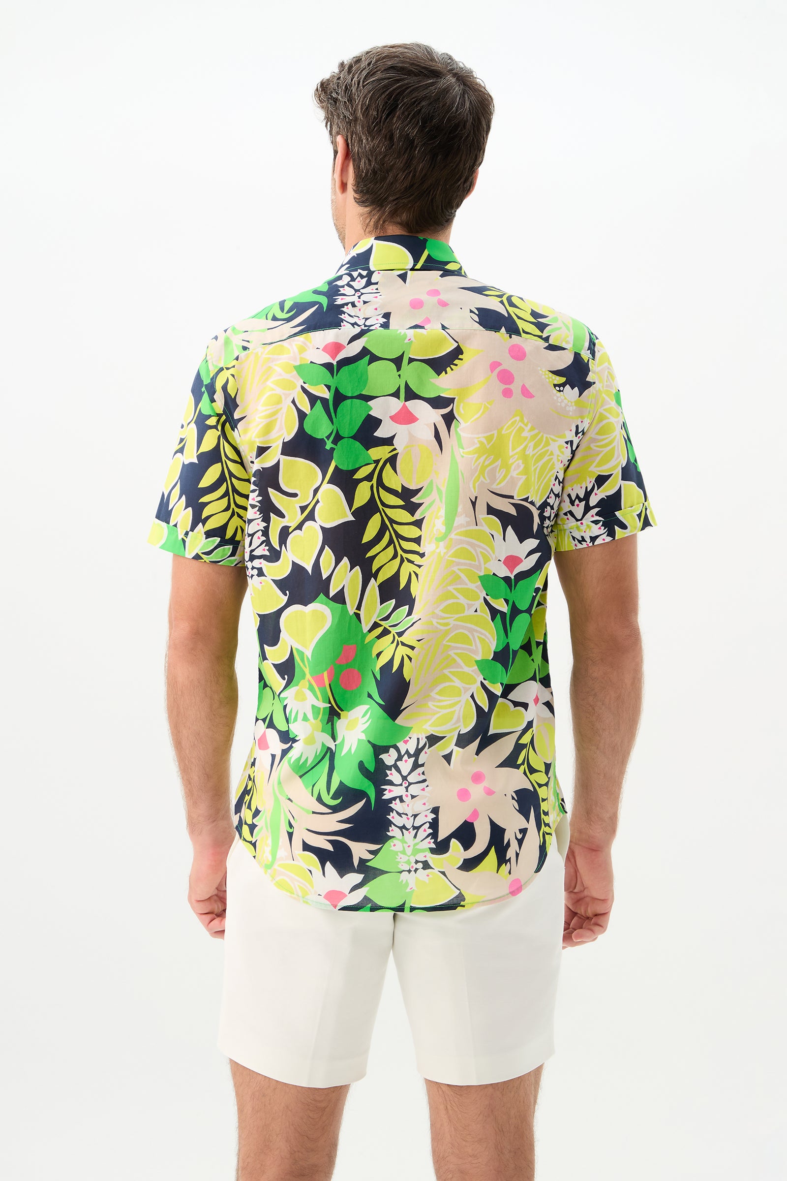 A man faces away wearing the Slim Jim Short-Sleeve Shirt, featuring a bold tropical leafy and floral pattern, paired with white shorts against a plain light background.
