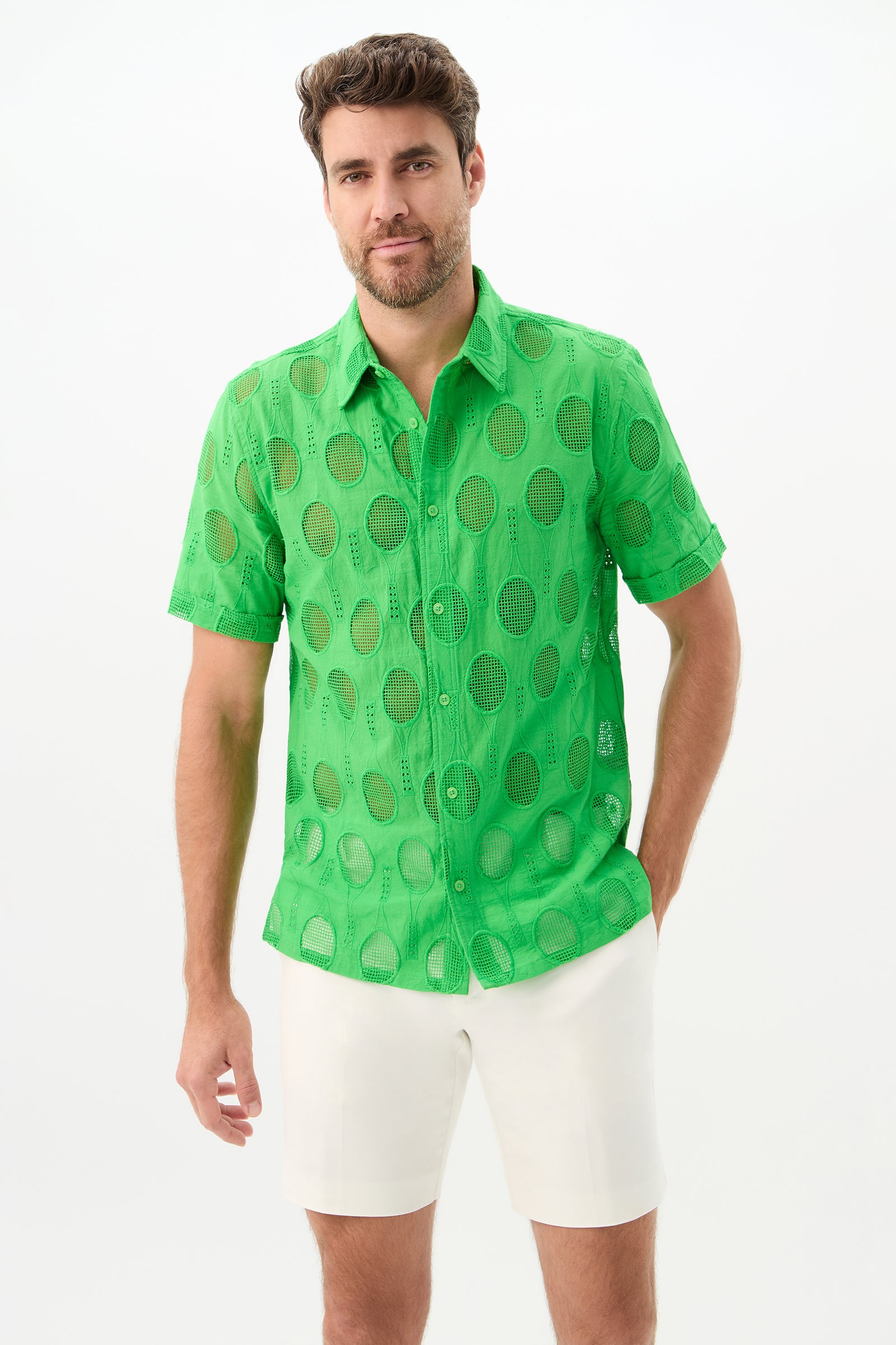 A man with brown hair and a beard wears the Branson Shirt - Tennis Eyelet in Grass Court Green over white shorts, standing against a plain white background.