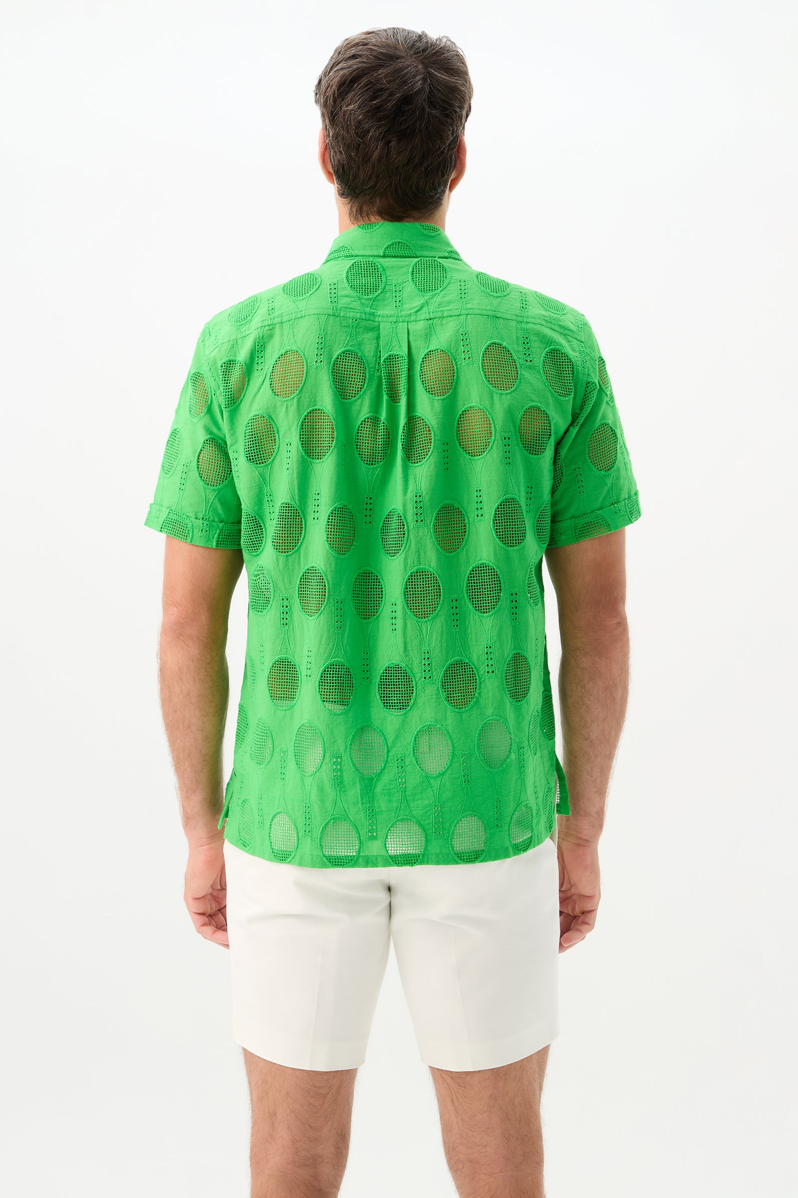 A man faces away, wearing the Branson Shirt - Tennis Eyelet in bright green with circular cutout patterns and white shorts. The background is plain white.