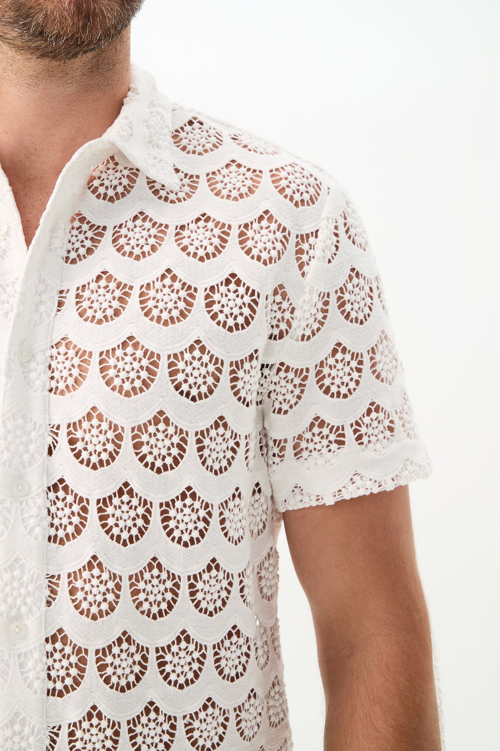 A person models the Branson Short-Sleeve Shirt - Crochet Lace, a white, see-through top with a scalloped pattern. Their chest and arm are partially visible against a plain white background.