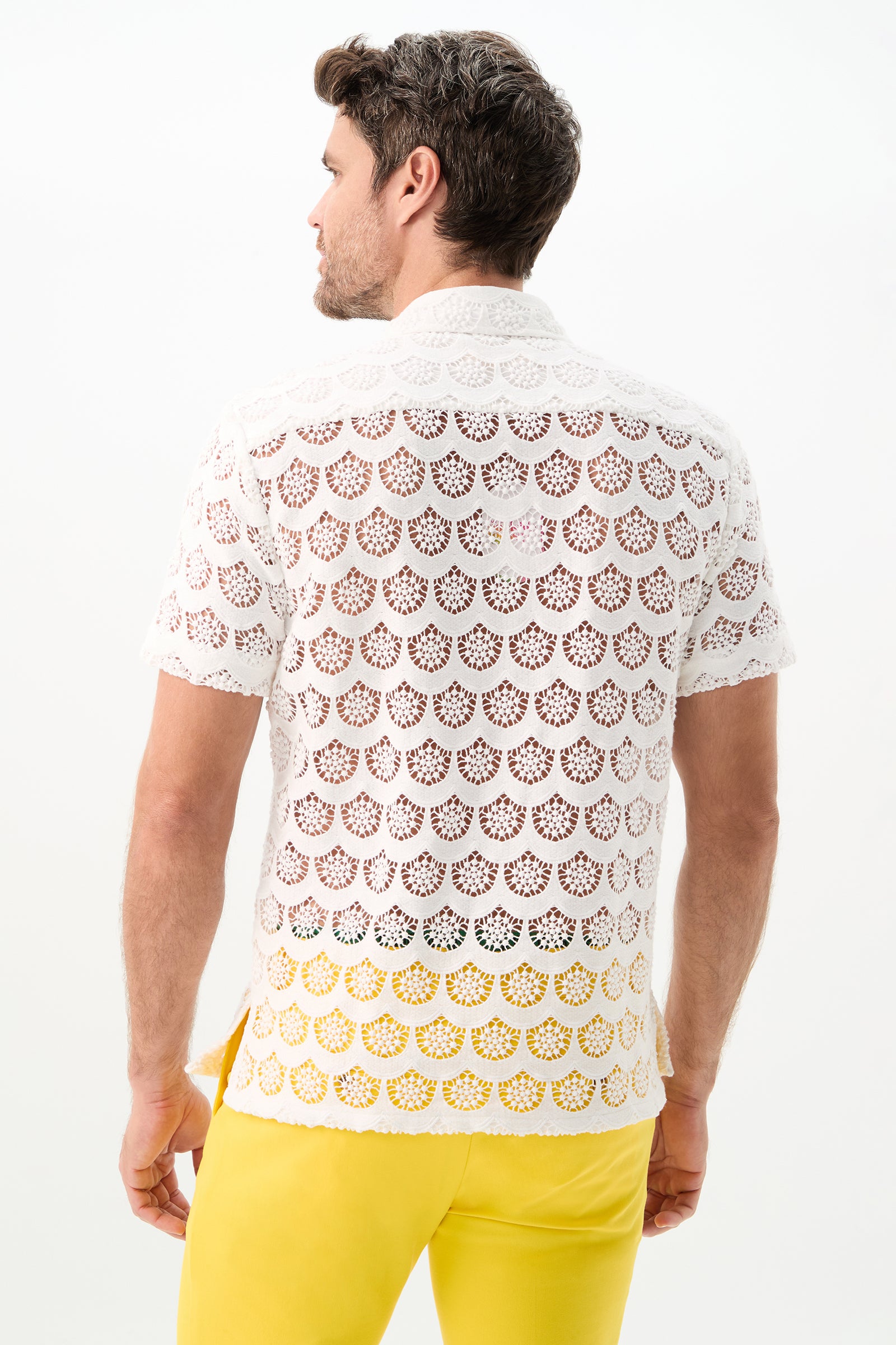 A man with short brown hair faces away, wearing the Branson Short-Sleeve Shirt - Crochet Lace in white and bright yellow pants, against a plain white background.
