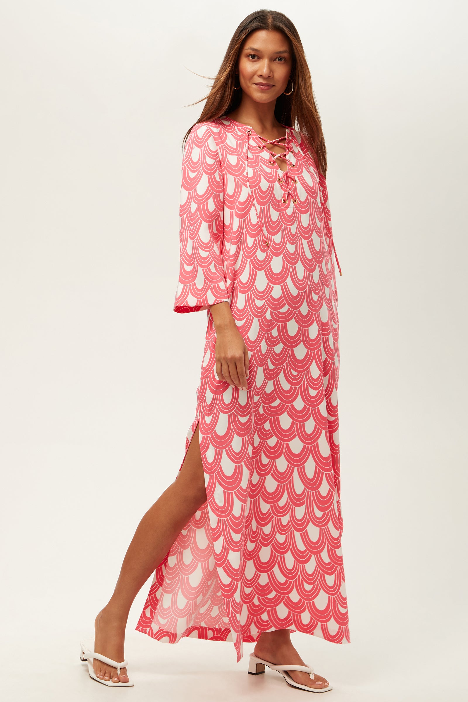A woman poses in the Catamaran 3/4-Sleeve Maxi Dress in Coral Crush/Whitewash, featuring a lace-up neckline and side slit. She has long, straight hair and completes the look with white sandals against a plain background.