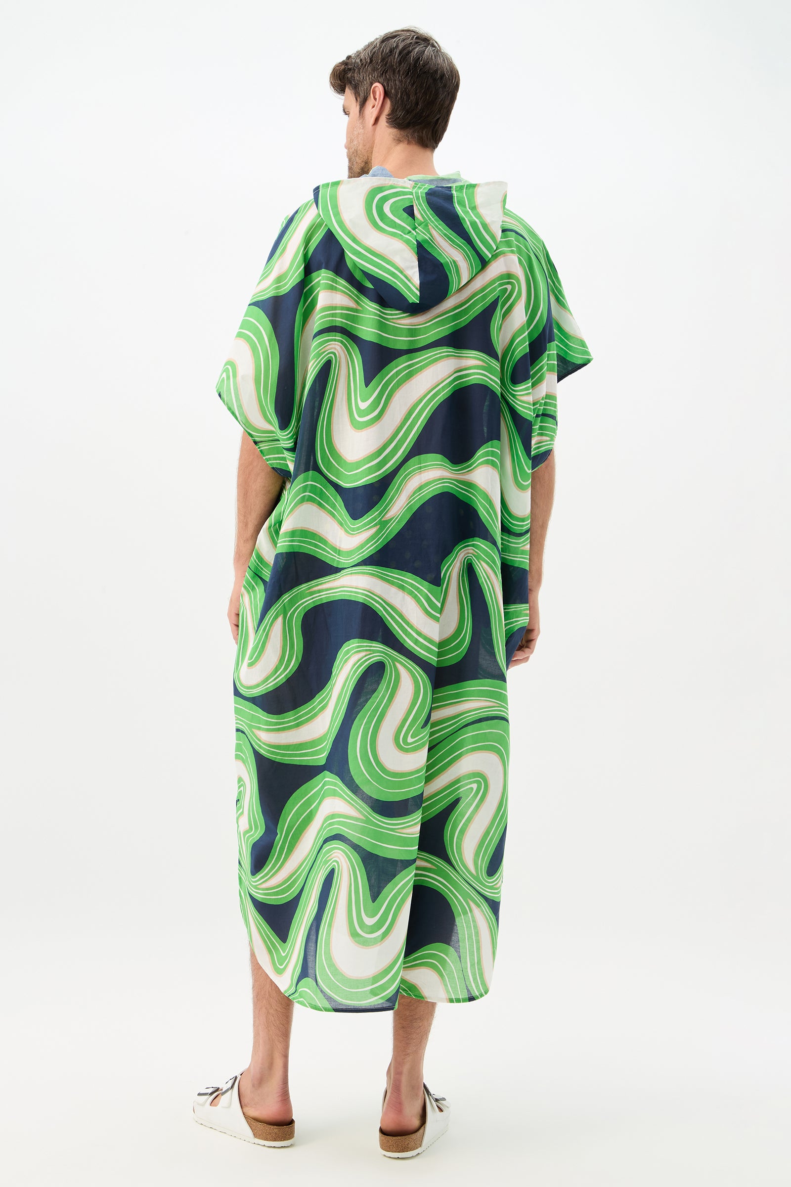 A person faces away, wearing the Hurley 2 Caftan - Serena Swirl, a loose-fitting, ankle-length hooded robe with green, blue, and white wavy patterns. The background is plain white.