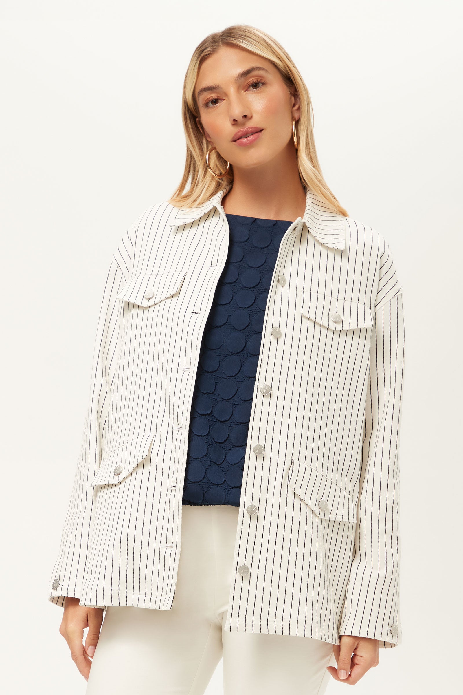 A person wears The Game Four-Pocket Jacket - Seles Stripe in Whitewash/Ink over a dark blue textured top and white pants, standing against a plain white background.