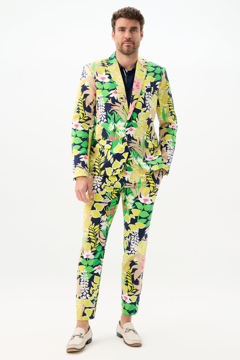 A man faces forward wearing the Thurston Blazer - PS Eternal, featuring a vibrant yellow, green, pink, and navy floral and leaf pattern. He has one hand in his pocket and wears light-colored loafers against a plain white background.