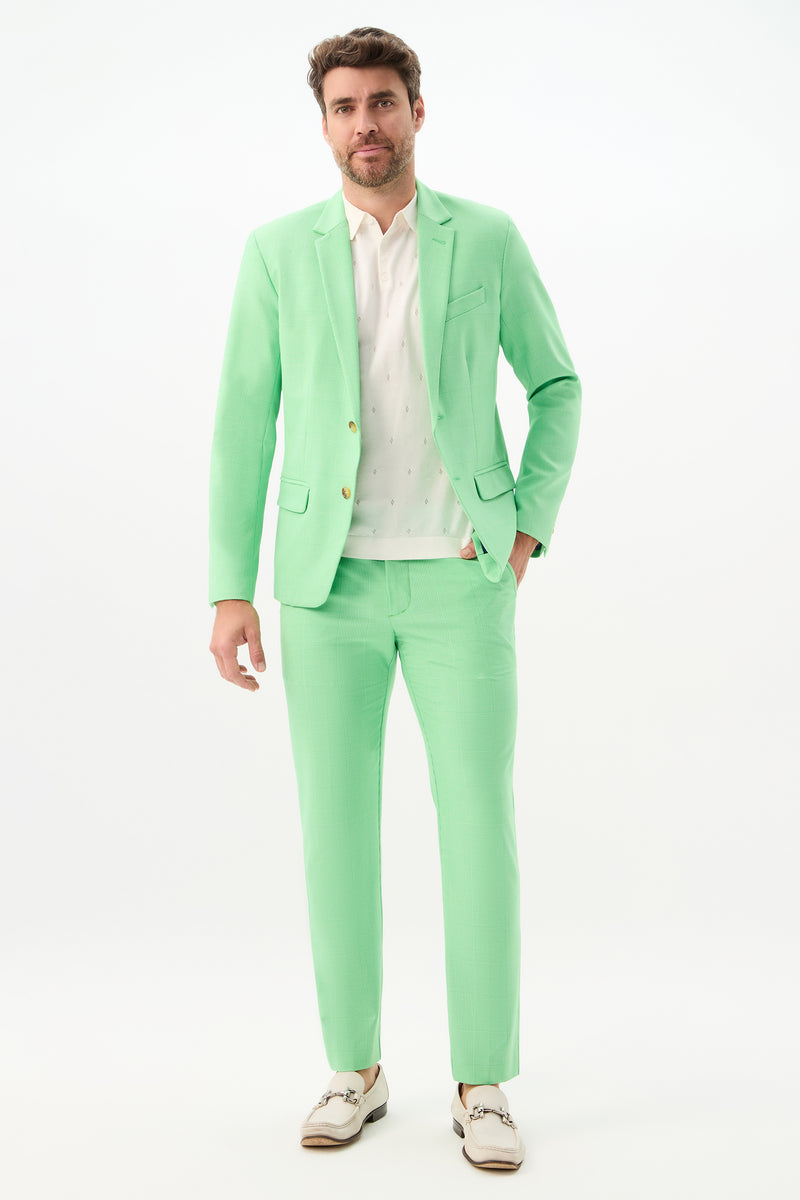 A man with short brown hair and a trimmed beard stands against a white background, wearing the Alex Slim Trouser - Game Time Glen Plaid, a patterned white shirt, and white dress shoes, looking relaxed.