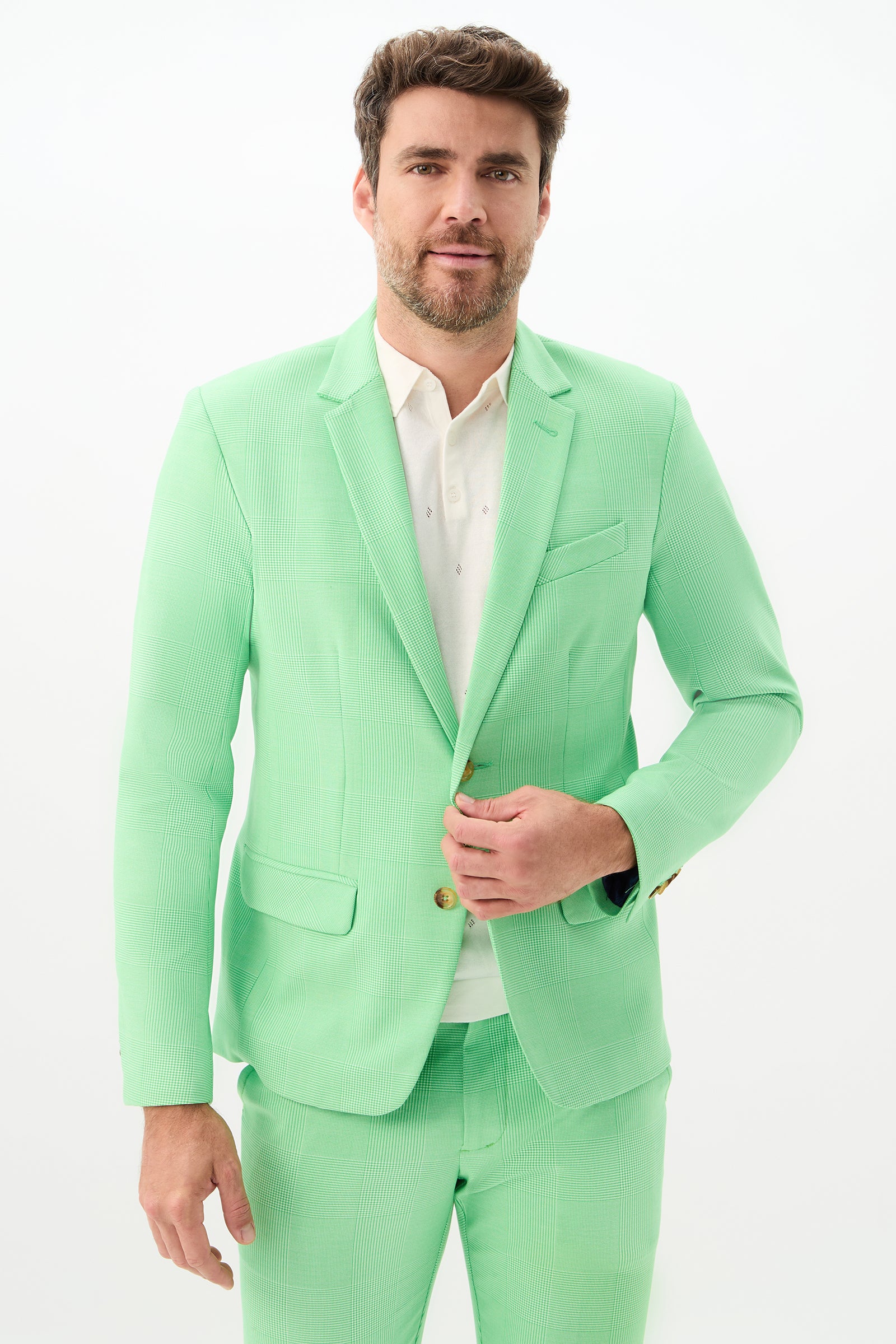 A man with short brown hair and a beard is wearing the Thurston Blazer - Game Time Glen Plaid in Grass Court Green/Whitewash over a white shirt, standing against a plain white background and buttoning his jacket.