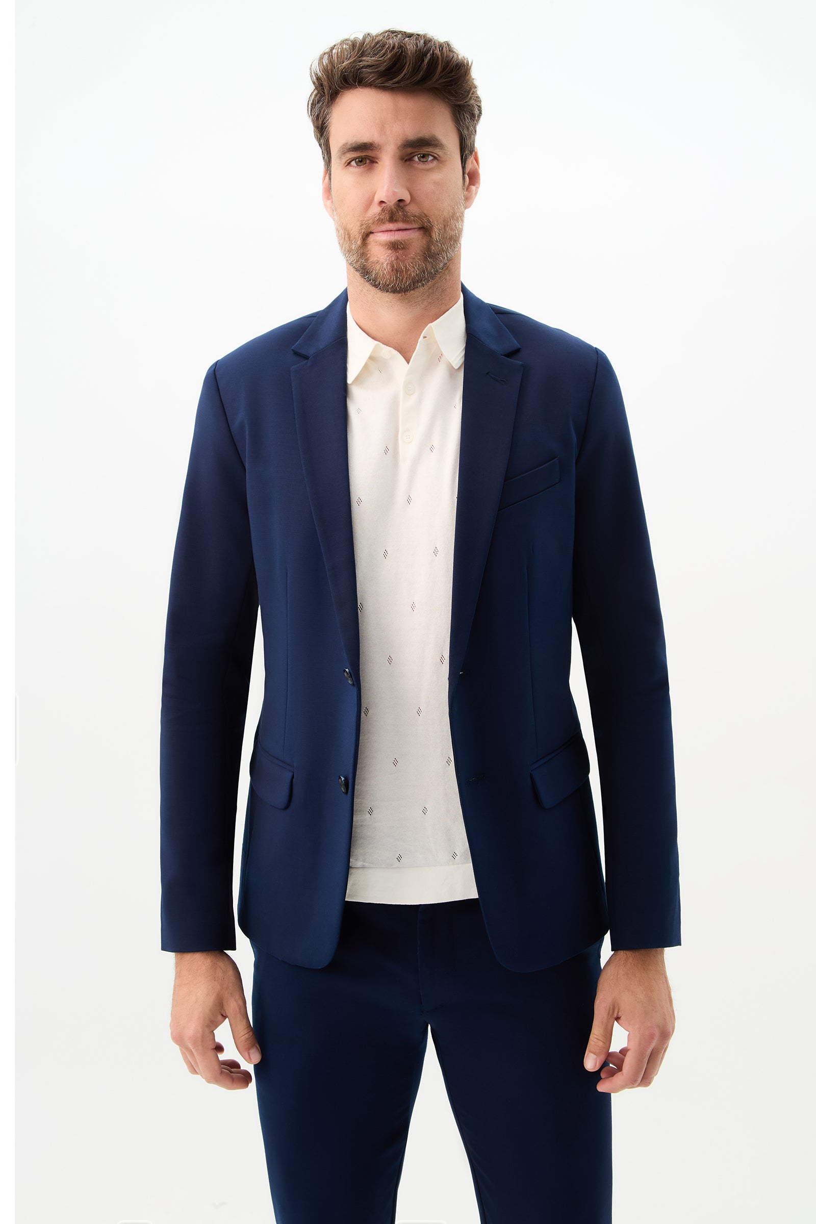 A man with short brown hair and a beard wears the Thurston Blazer - Solid Suiting in Ink with matching pants over a subtly patterned white shirt, standing against a plain white background.
