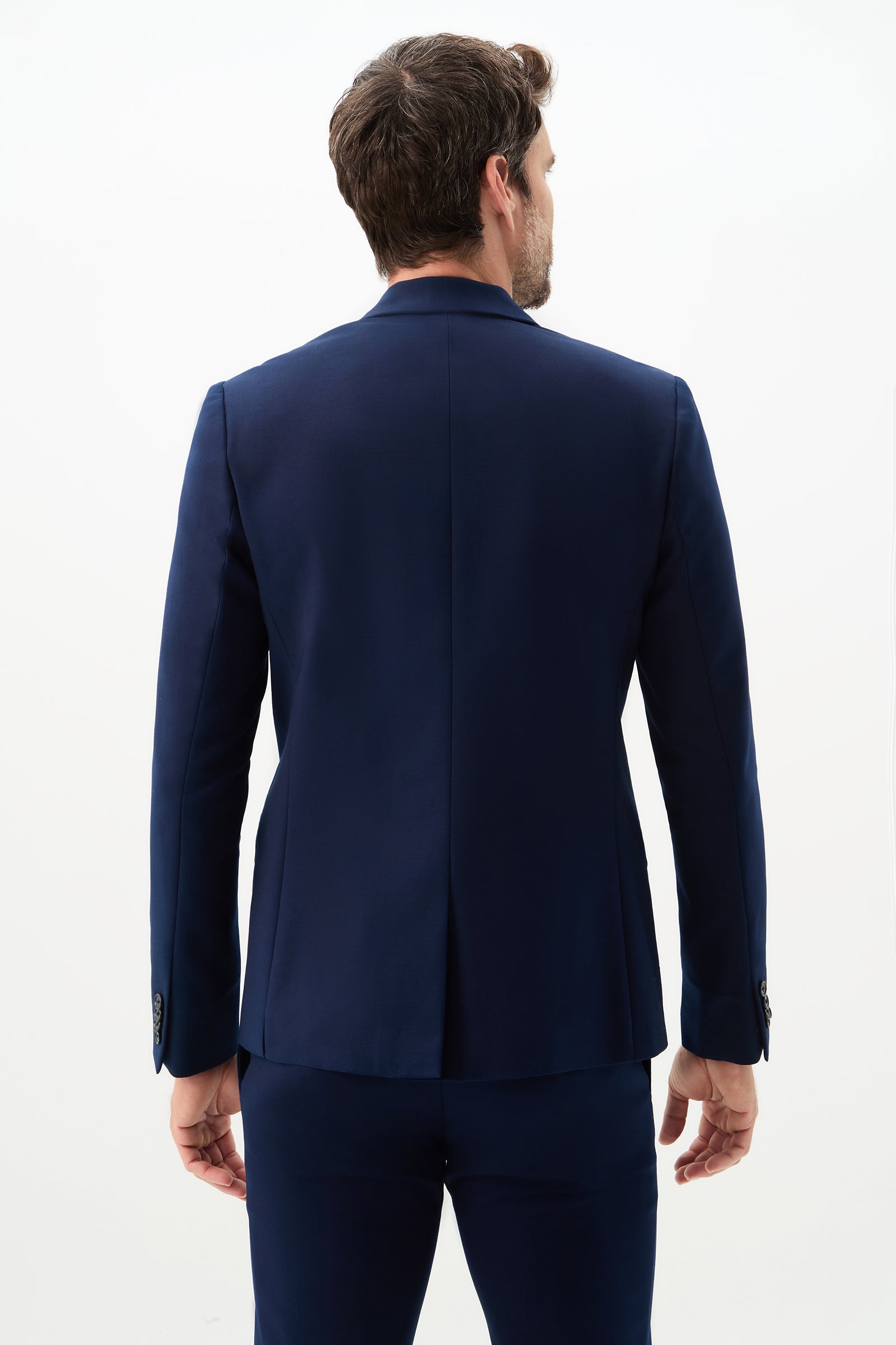 A man with short brown hair stands with his back to the camera, wearing the Thurston Blazer - Solid Suiting in dark blue against a plain white background.