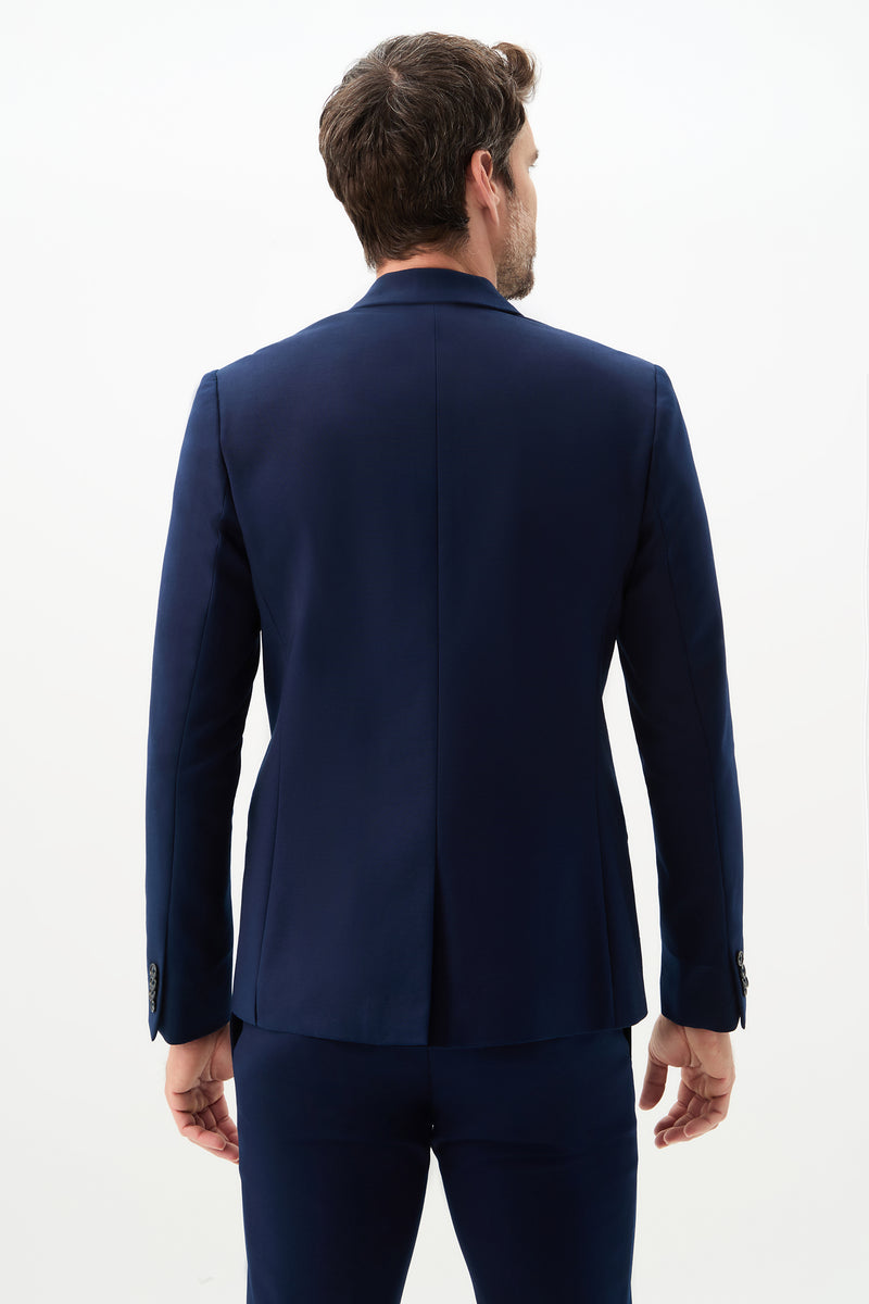 A man with short brown hair stands with his back to the camera, wearing the Thurston Blazer - Solid Suiting in dark blue against a plain white background.
