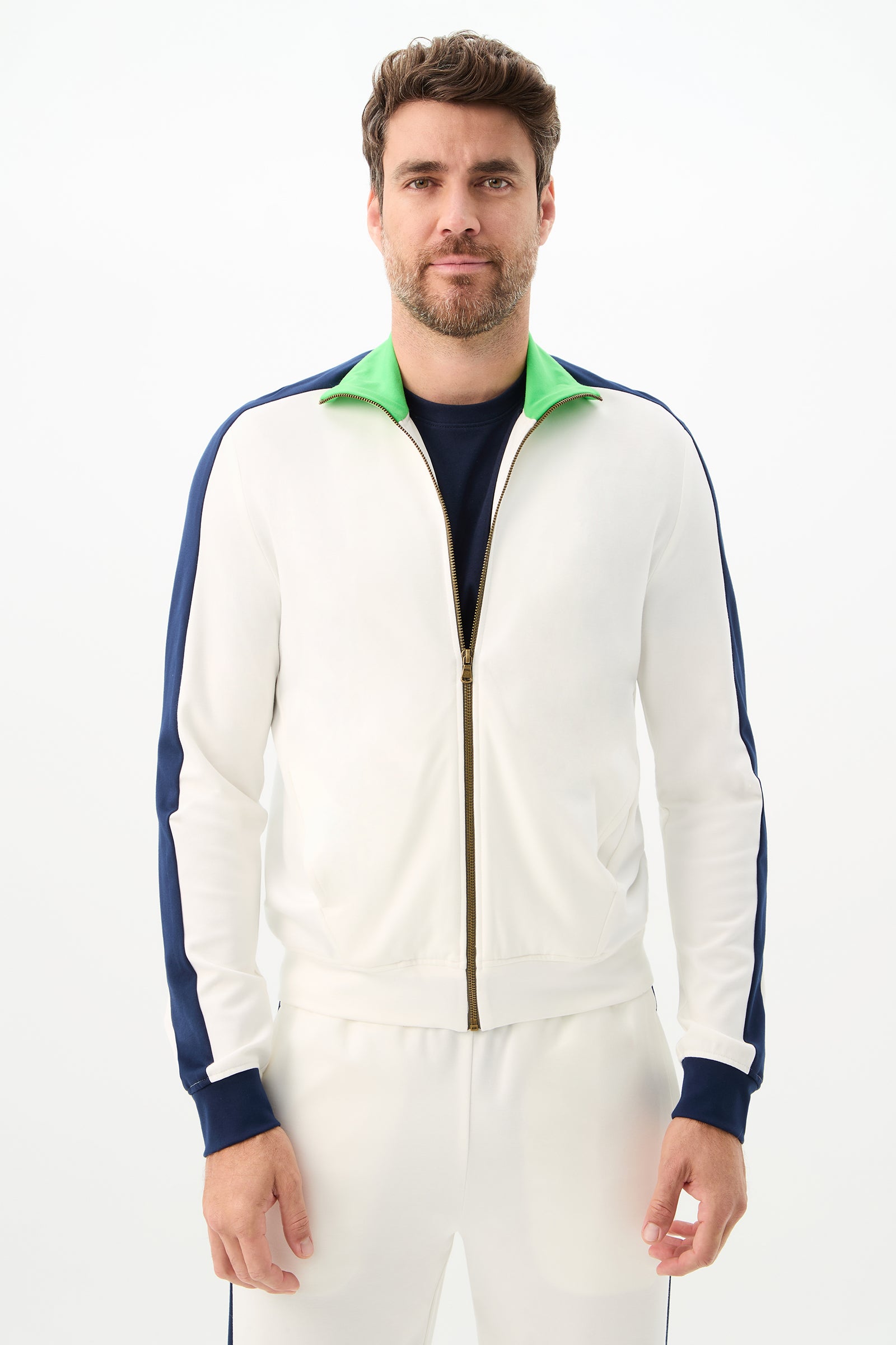A man with short brown hair and a beard wears the Ugo Track Jacket - Cozy Ponte in Multi, paired with matching white pants, standing against a plain white background and looking at the camera.