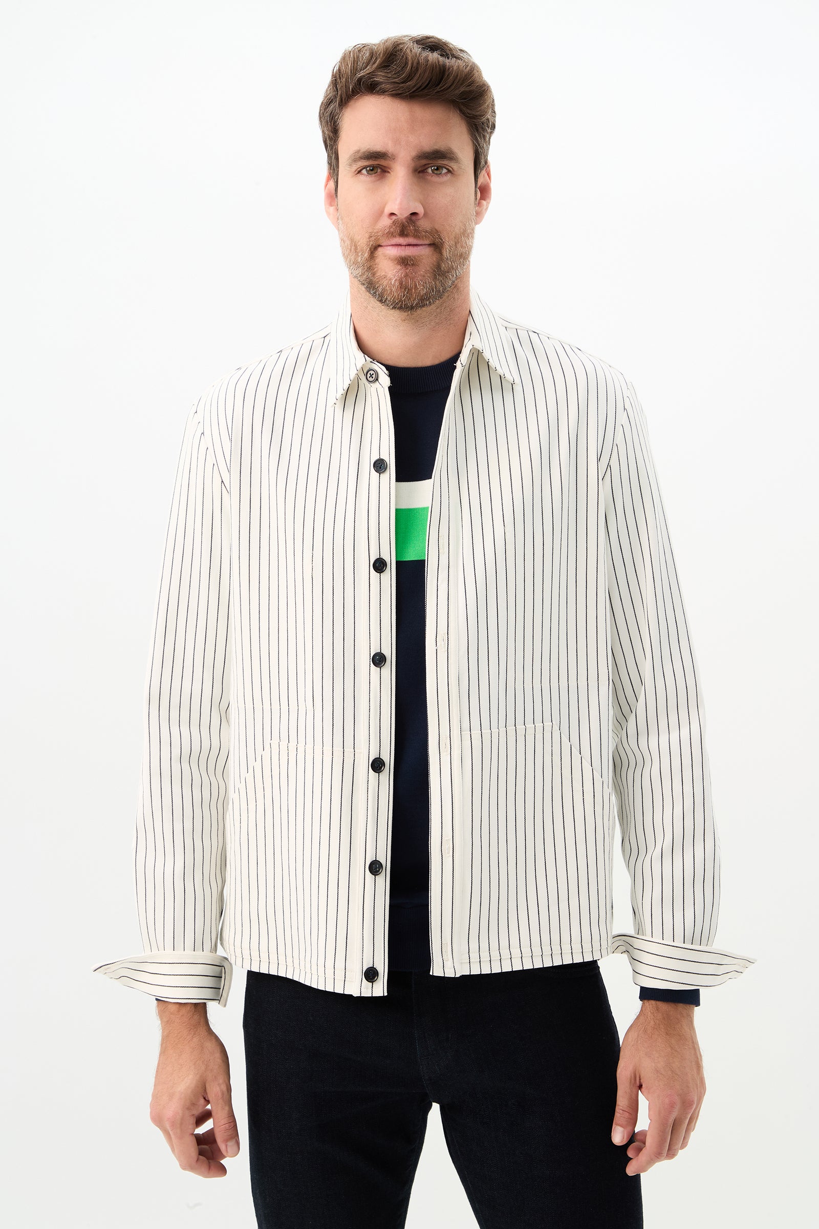 A man with short brown hair and a beard wears the Mulholland Shirt Jacket in Seles Stripe, color Whitewash/Ink, over a dark shirt and dark pants, standing against a plain white background.