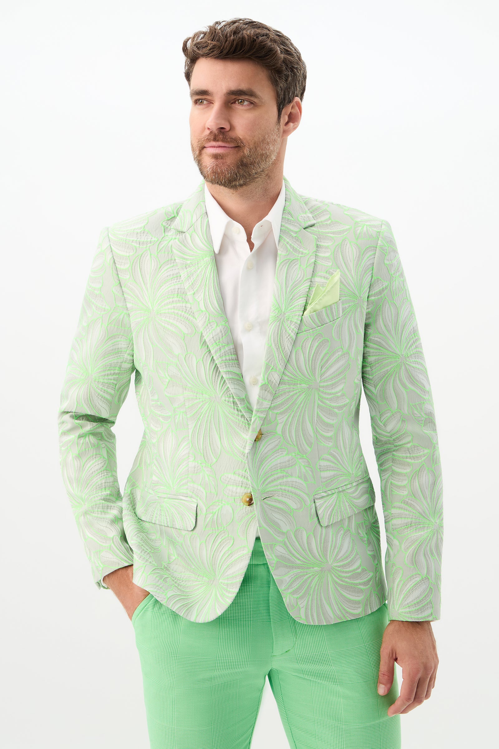 A man with short brown hair and a beard wears the Thurston Blazer - Hibiscus Jacquard in Vert over a white dress shirt and bright green pants, standing against a plain white background.