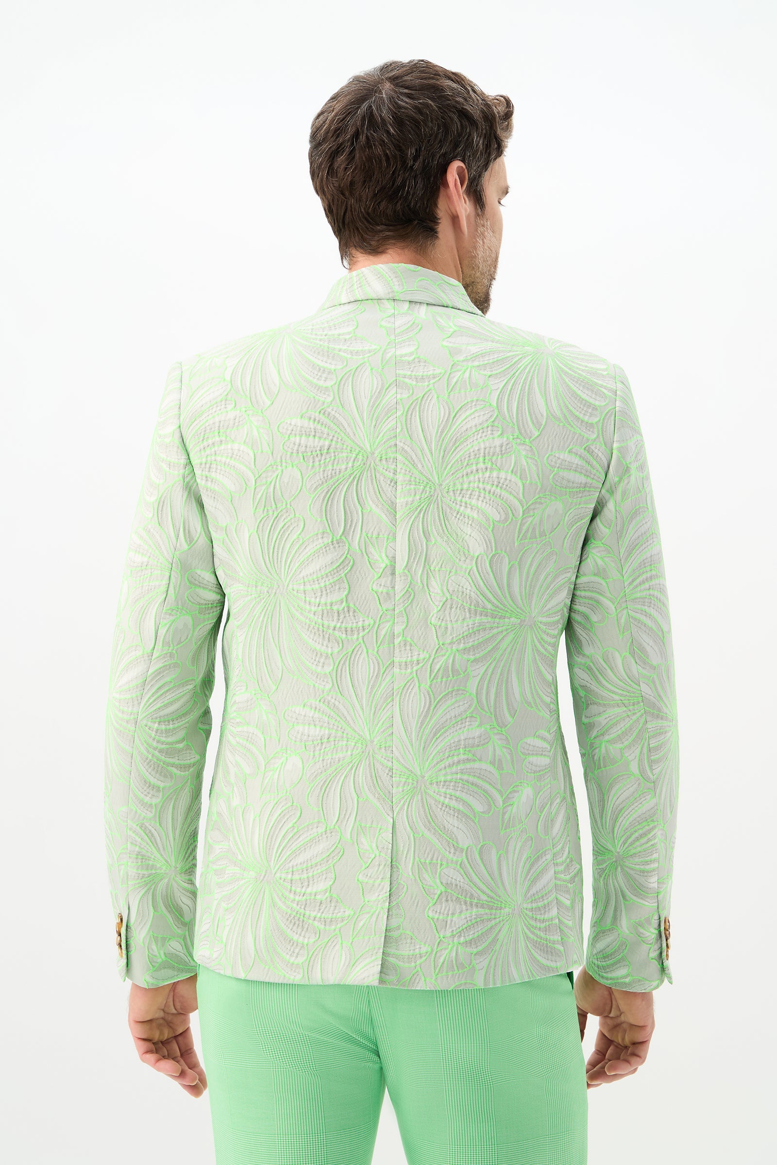 A man stands facing away, wearing the Thurston Blazer - Hibiscus Jacquard in light green with a swirling floral pattern and matching mint green pants against a plain white background.