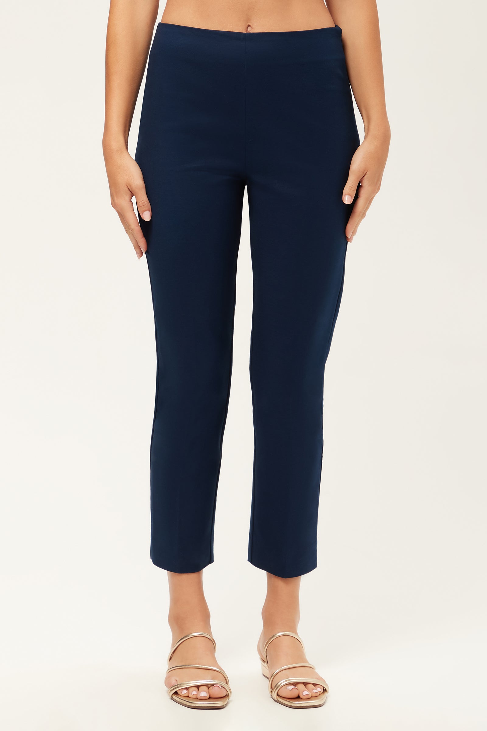 A person wearing the Tie Breaker Slim Crop Pant - Solid Suiting in Ink and beige sandals stands against a plain, light background, with only the lower half of their body visible.