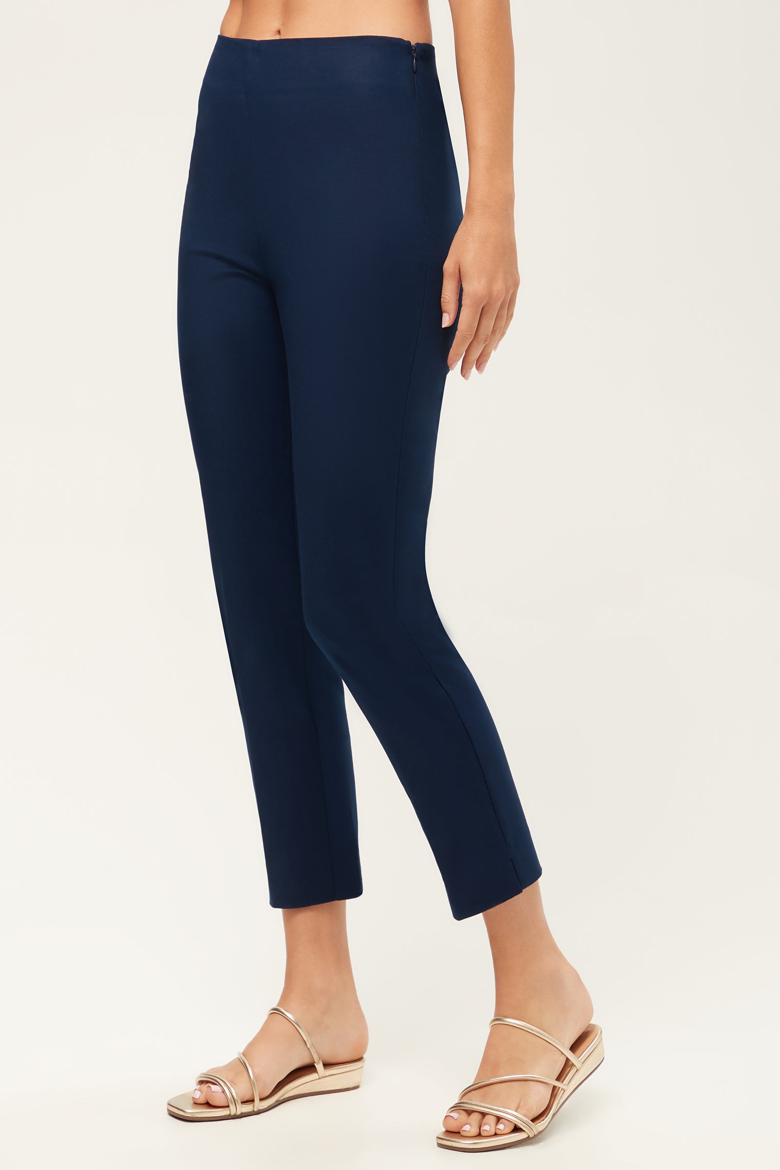 A person wearing Tie Breaker Slim Crop Pant - Solid Suiting in navy with beige flat sandals stands against a plain light background, with only the lower half of their body visible.