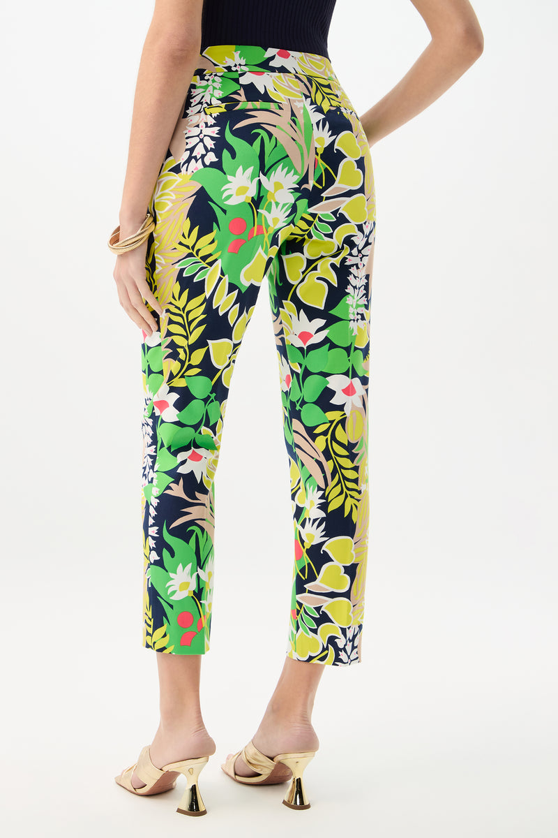 A woman faces away, wearing the Aubree 2 Pant - PS Eternal, a high-waisted, slim-fit style with a vibrant floral and leaf print. She pairs it with cream heeled sandals and a black sleeveless top against a plain white background.