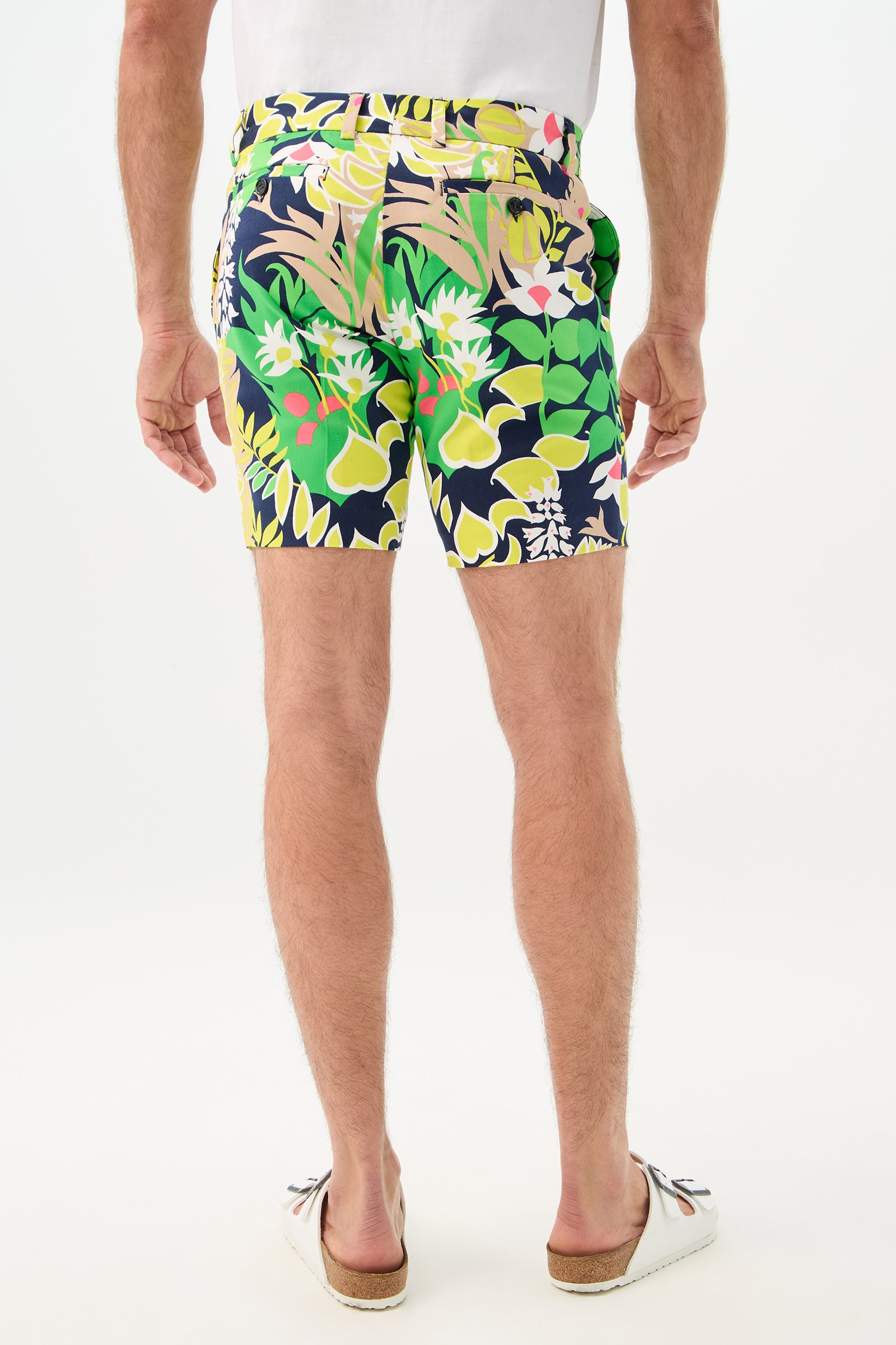 A man stands with his back turned, wearing a white T-shirt, Lawrence Short - PS Eternal featuring a colorful floral pattern, and white slip-on shoes against a plain white background.