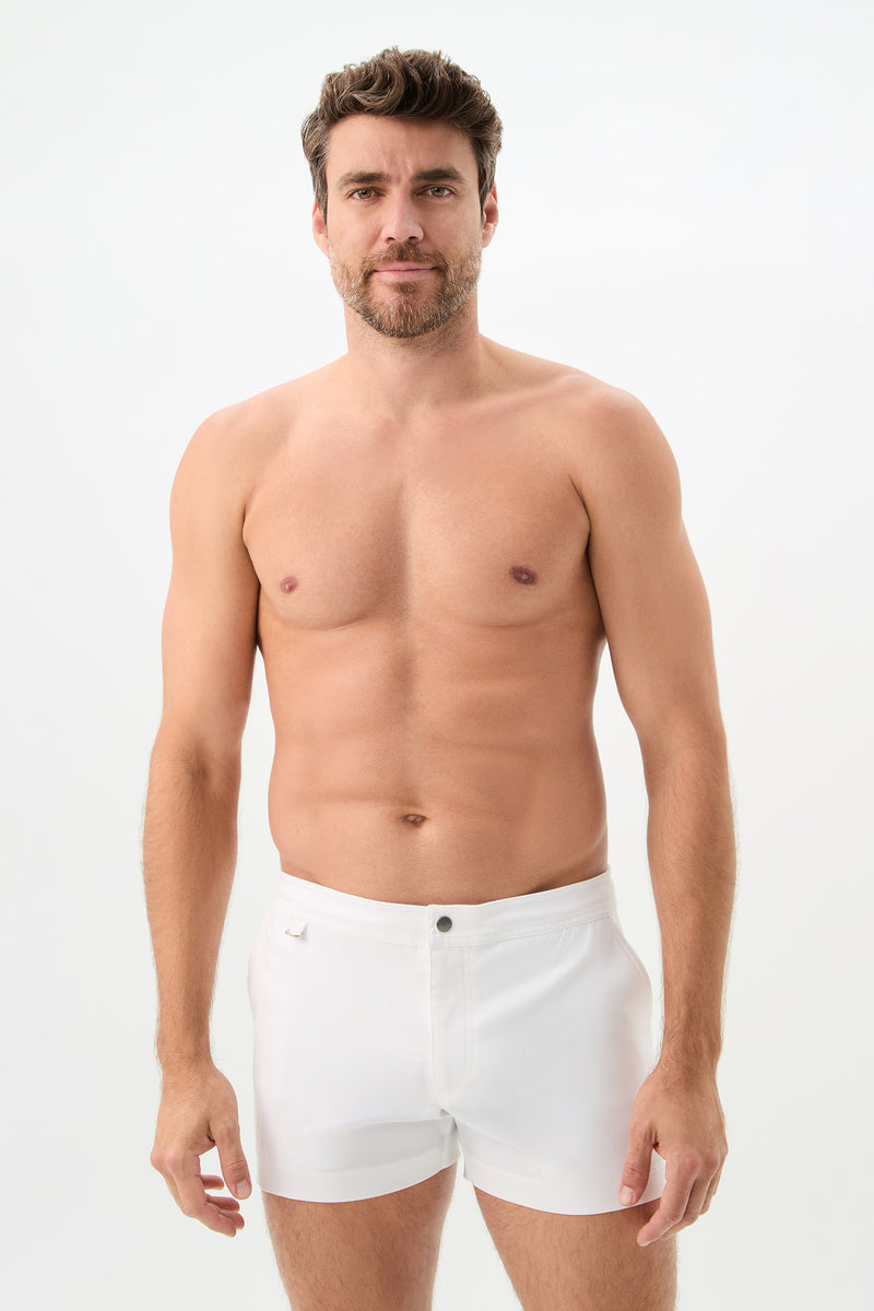 A man with short brown hair and a beard stands against a white background, wearing the Chico Swim Trunk - Lemar Solid in white. He is shirtless and looks at the camera with a neutral expression.